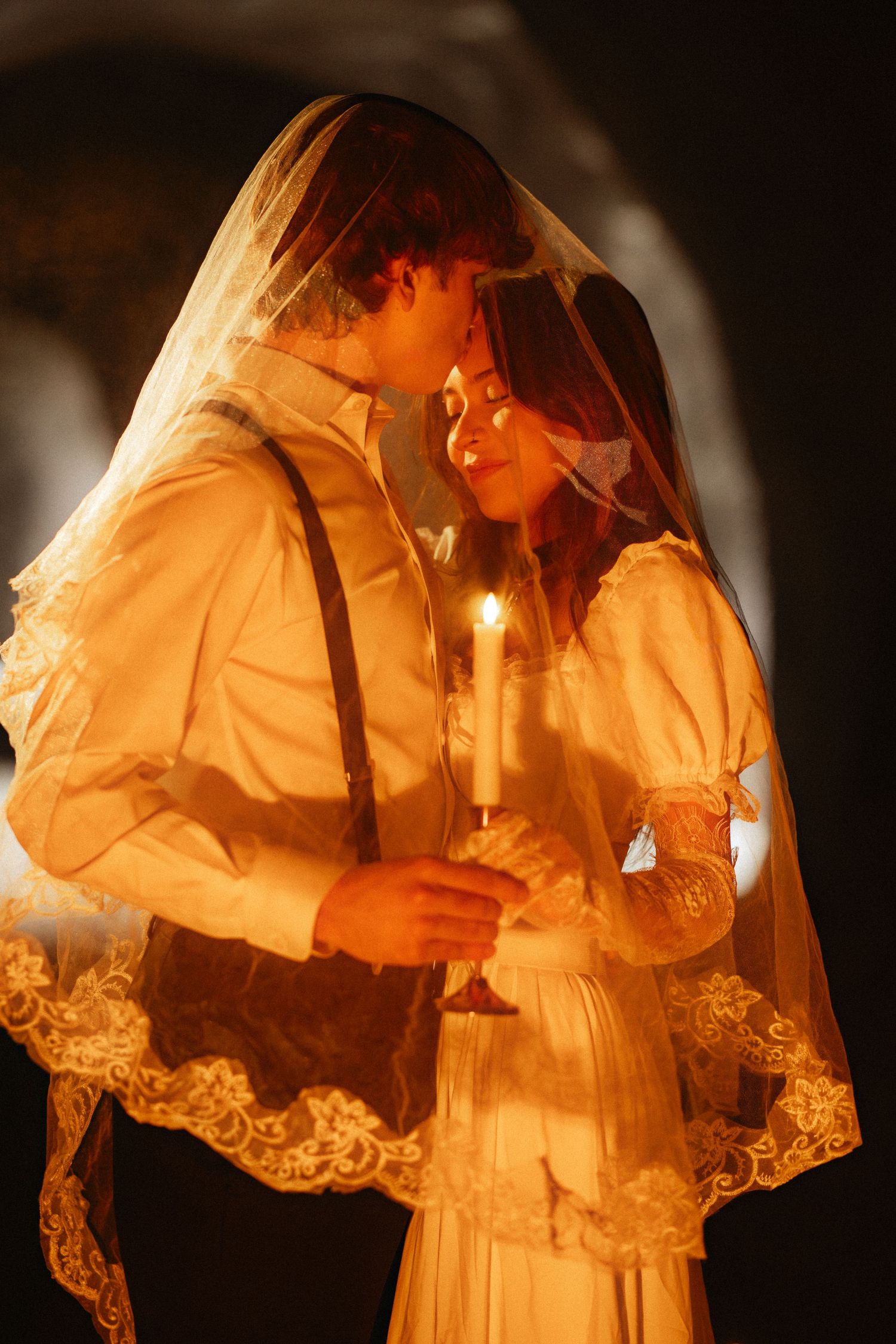 Ethereal figures in white lace dresses illuminated by candlelight create a dreamy, romantic atmosphere.