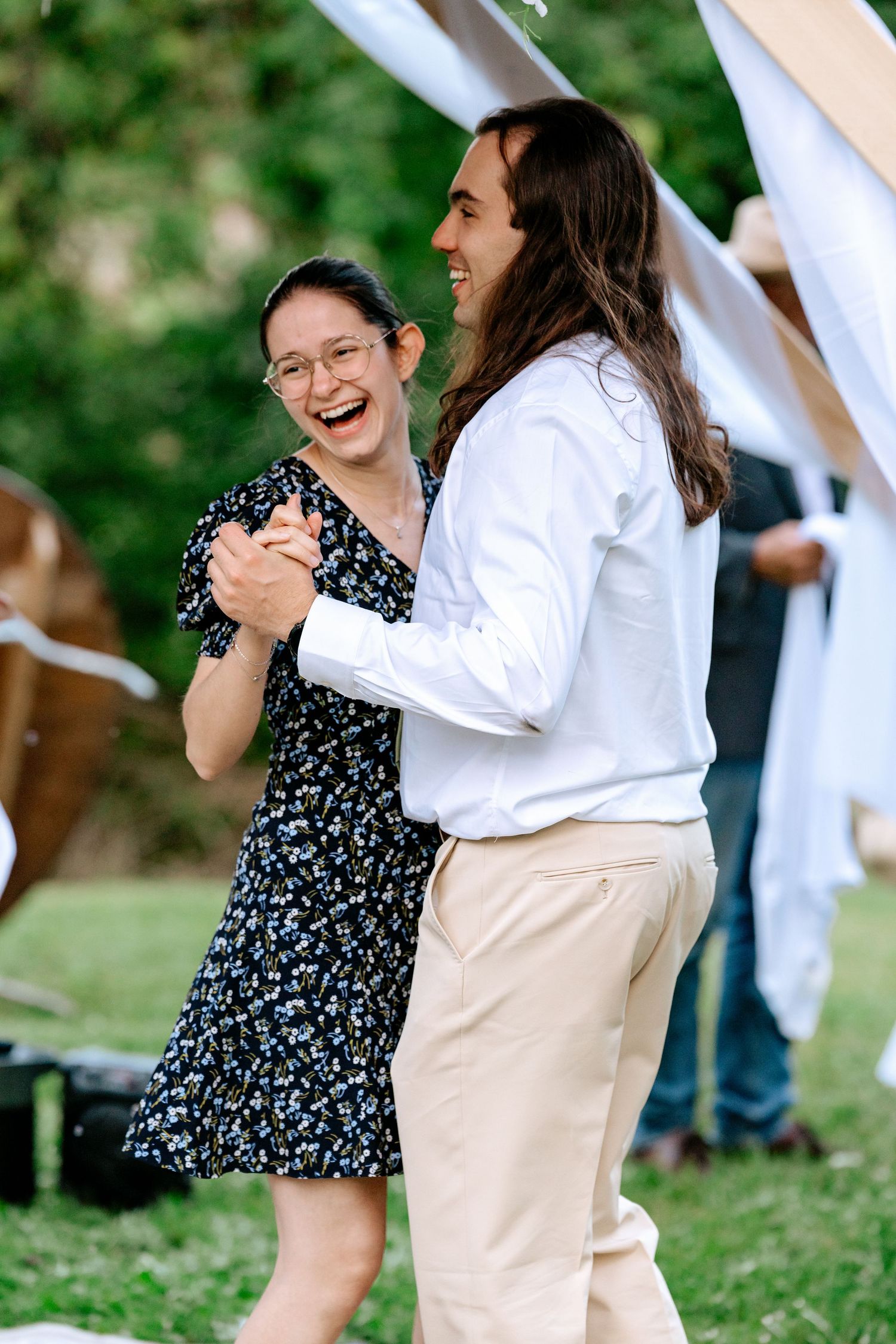 Couple laughing and dancing together at an outdoor wedding reception in garden.