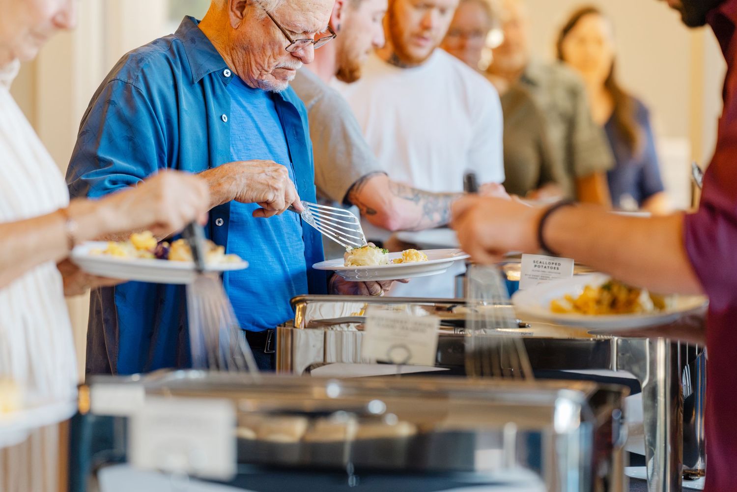 Guests serving themselves at a wedding reception buffet line with various food dishes.