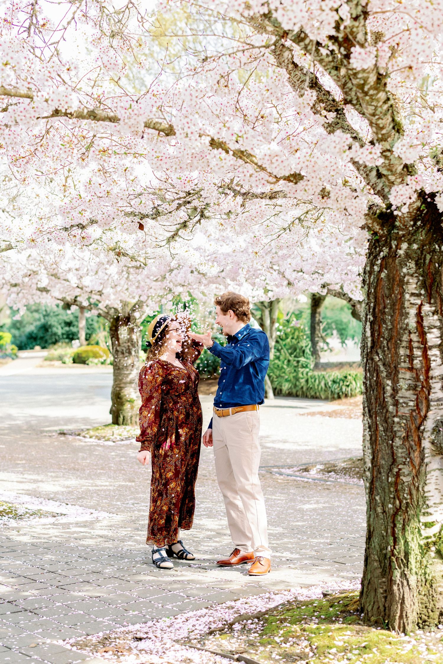 A couple shares a romantic moment under blooming cherry blossom trees in a spring garden setting.