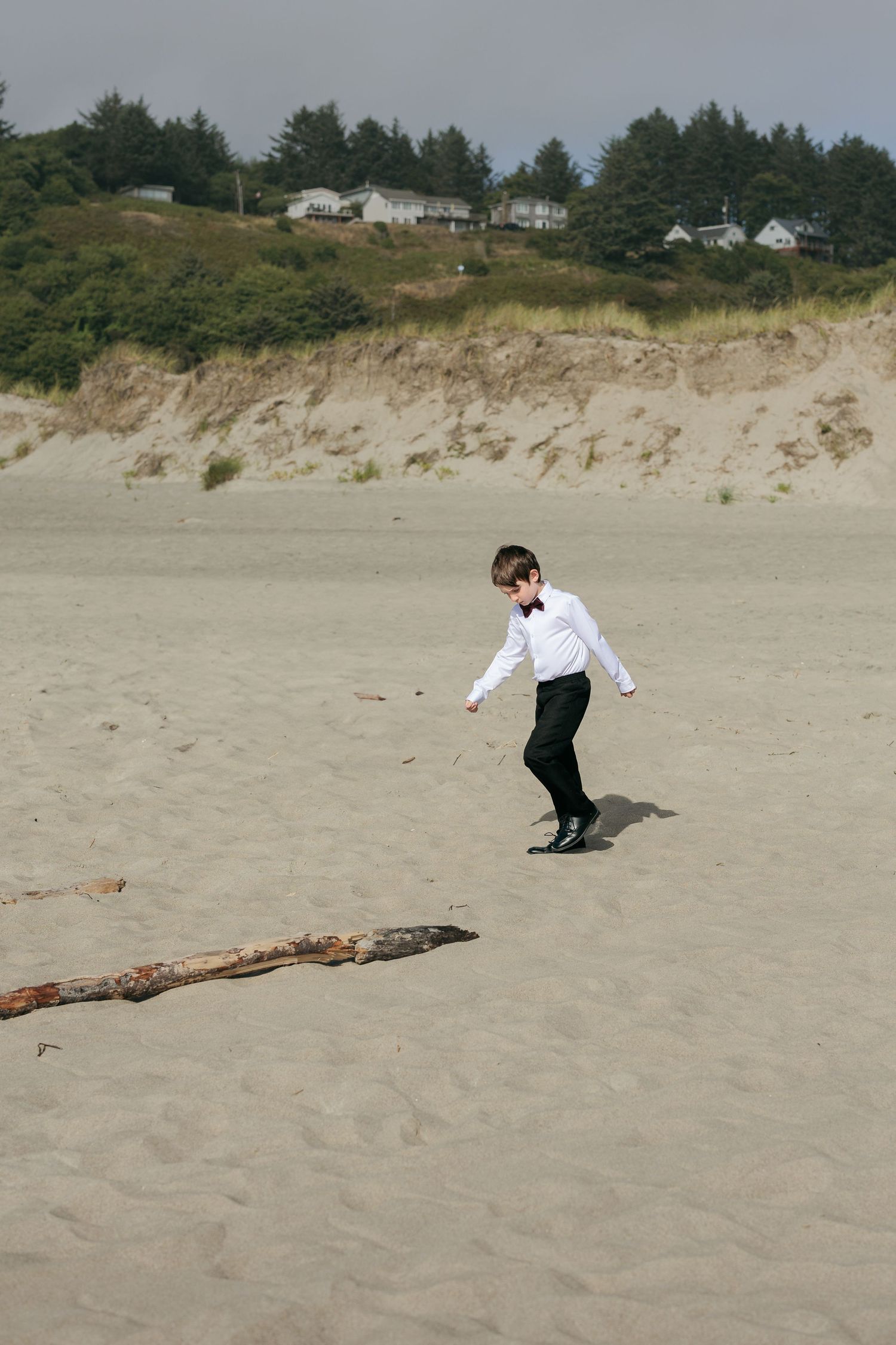 A person in formal attire plays on a sandy beach with coastal houses on the cliffs behind.