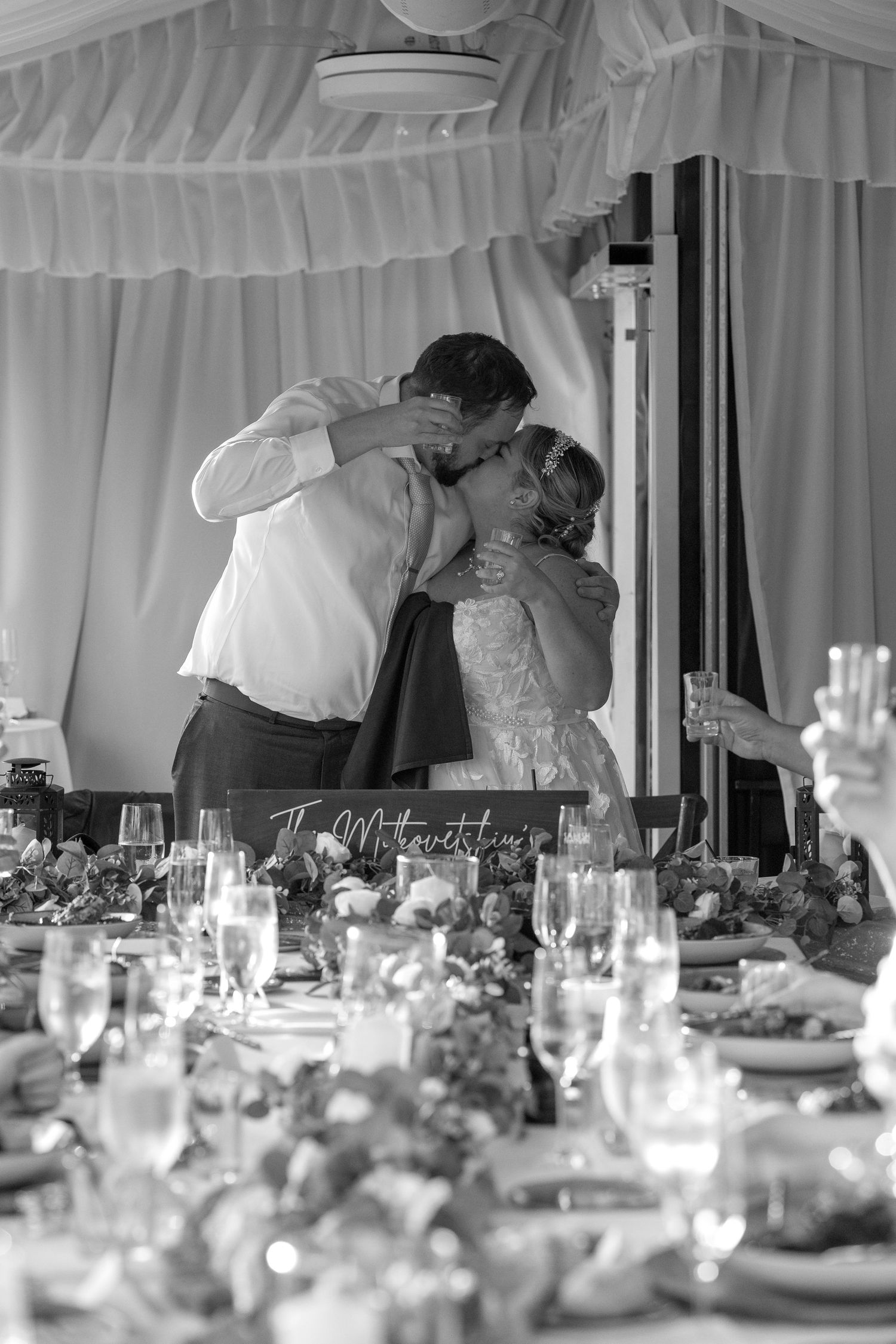 A romantic moment captured at an elegantly set wedding reception with glassware and decorations on the tables.