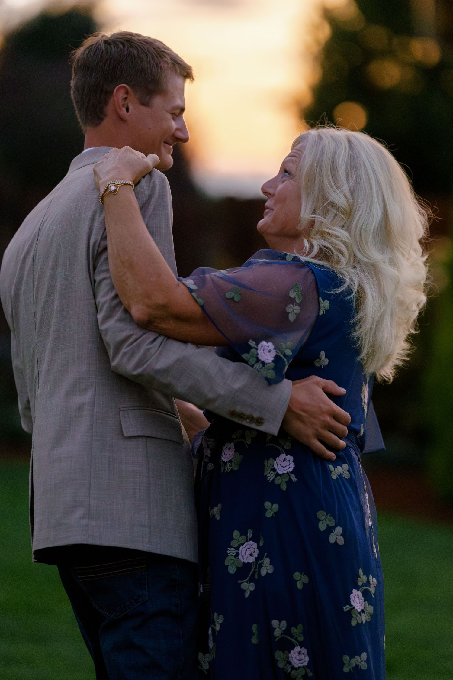 A couple shares a tender dance moment during sunset at an outdoor reception.