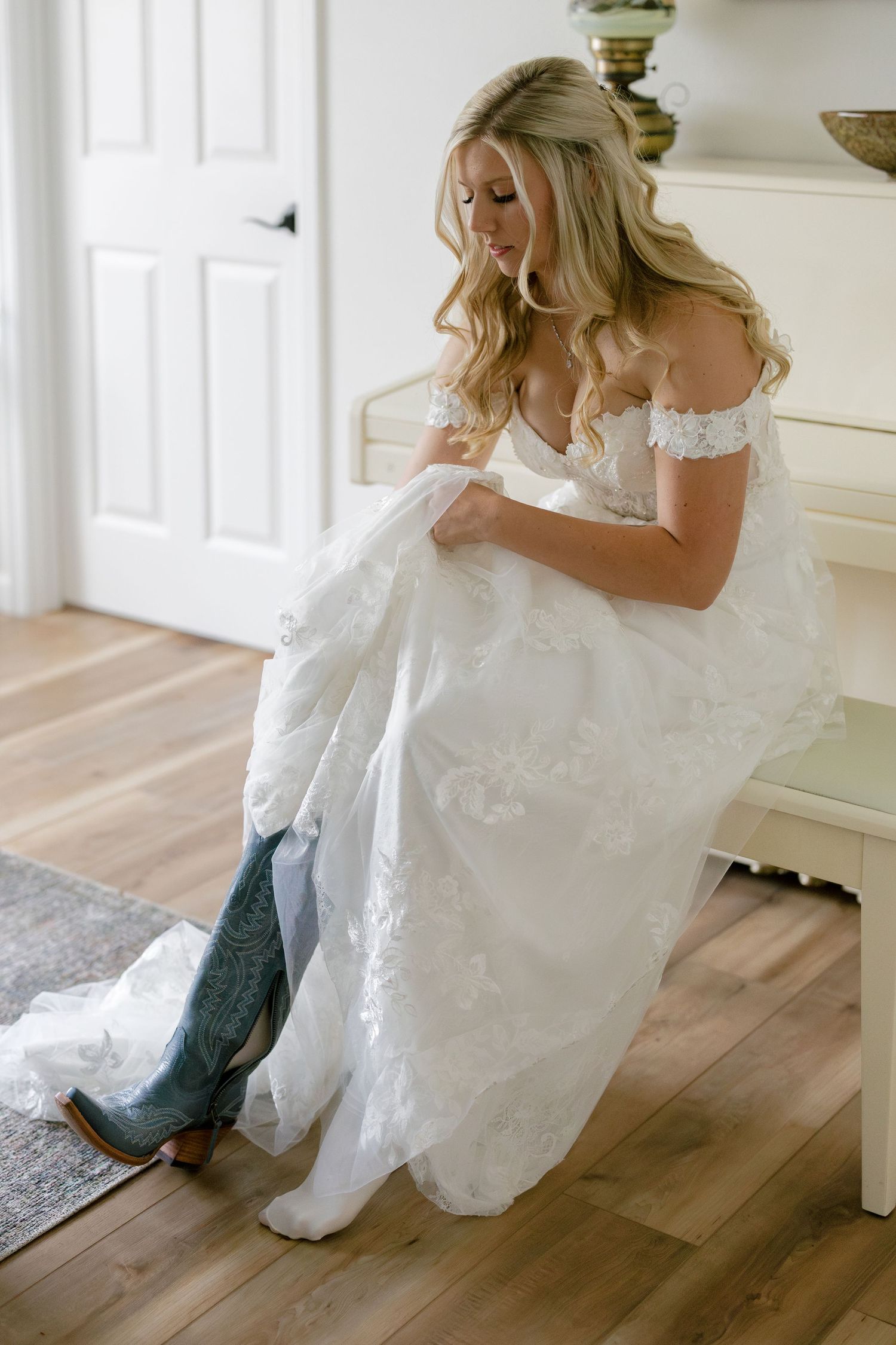 Someone in a white wedding dress sitting on hardwood floors putting on boots.
