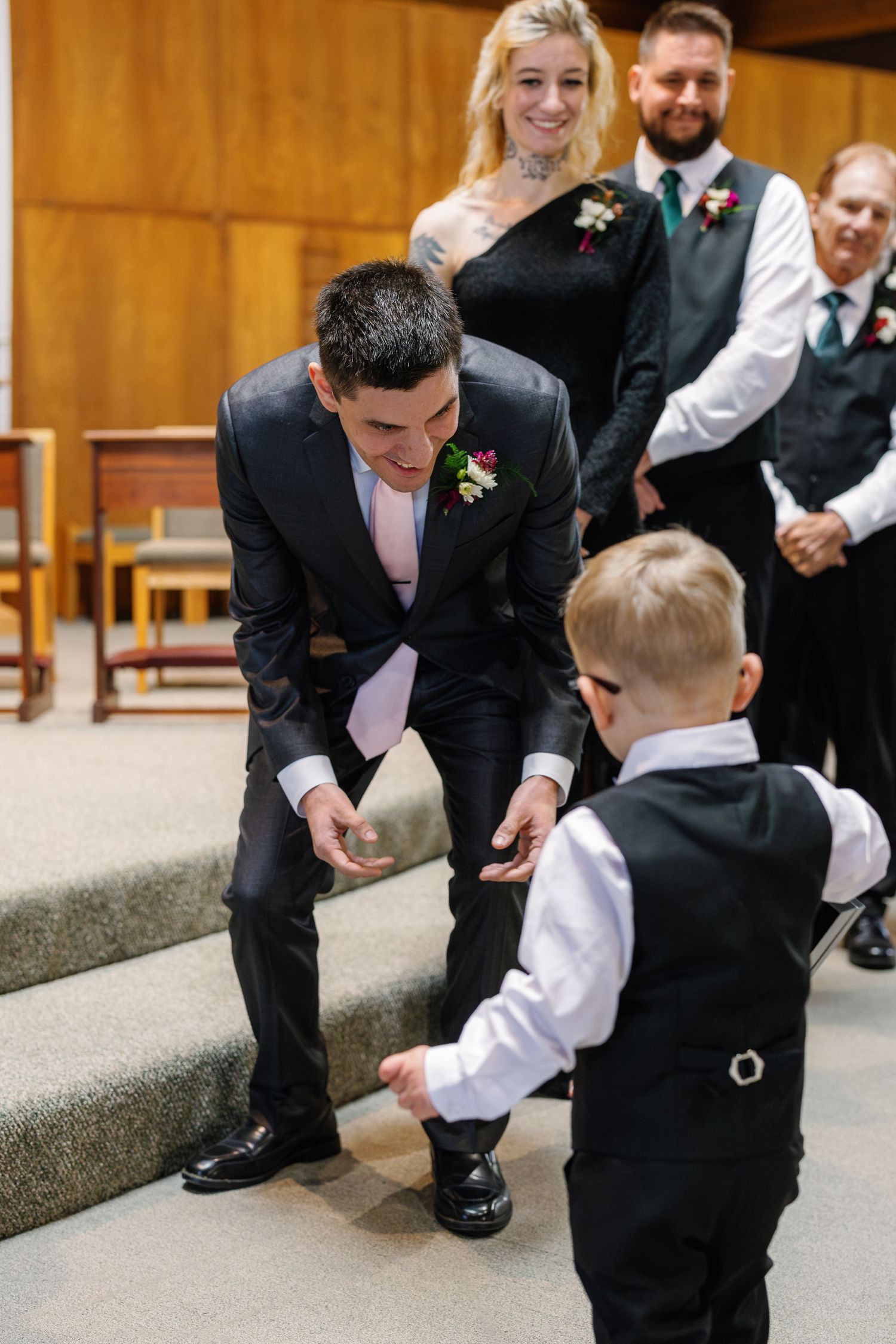 A sweet moment during a wedding ceremony as a man in a suit bends down to interact with a small boy in formal attire.