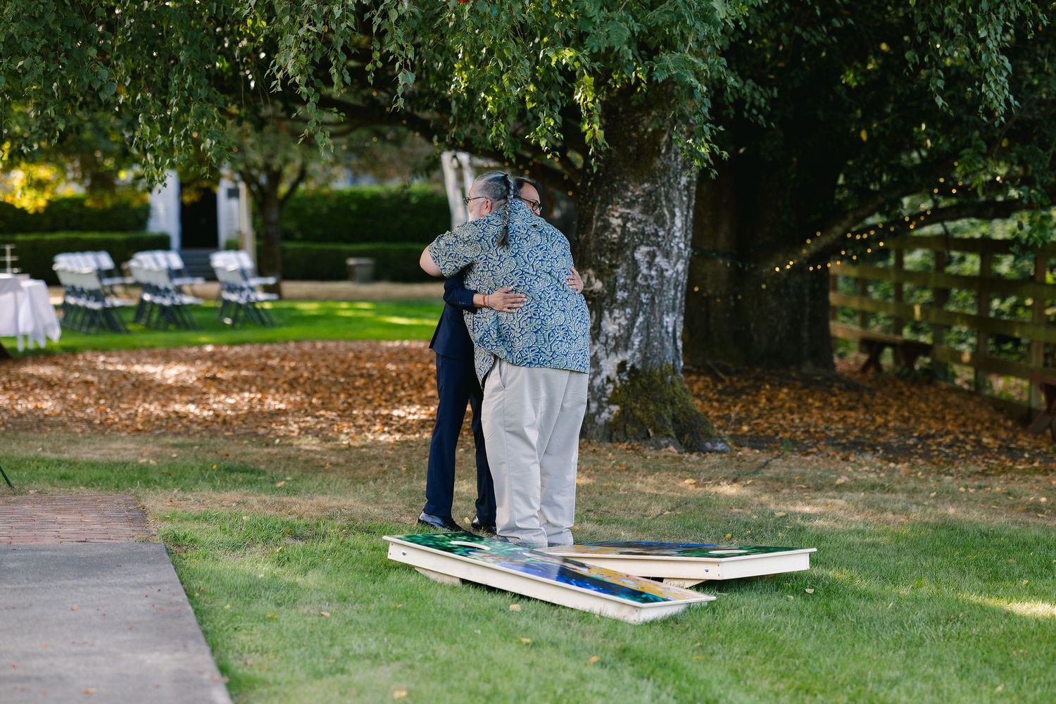 Outdoor wedding setup with cornhole boards and trees in a garden setting.