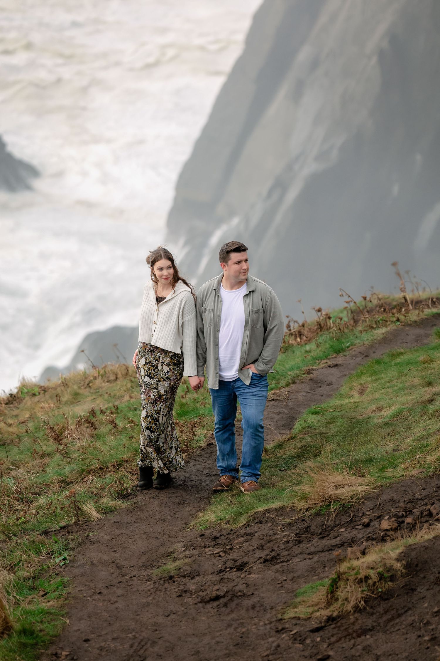 A couple walks along a scenic coastal cliff path with dramatic ocean views.
