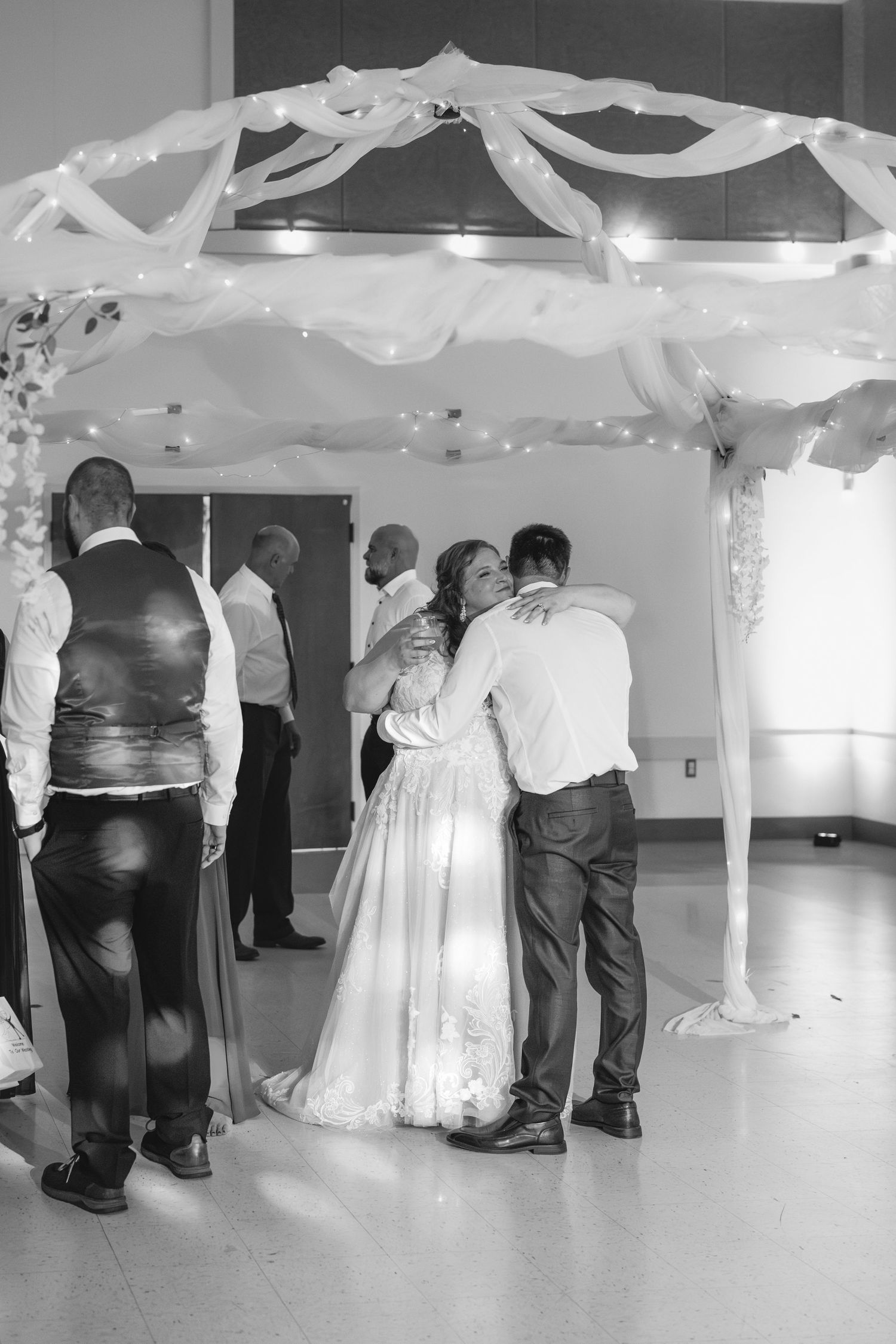 A tender moment under decorative white fabric draping at an indoor celebration.