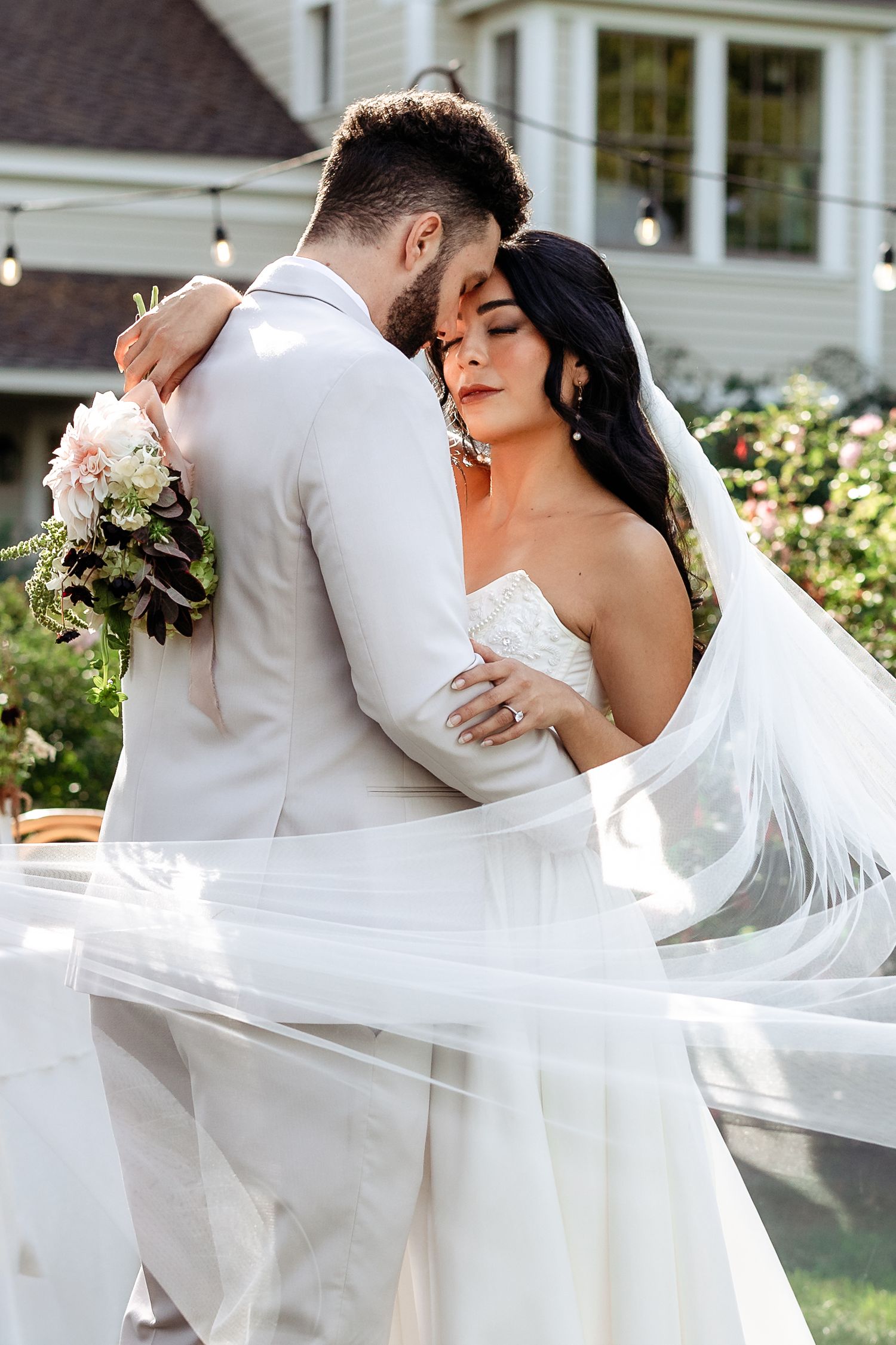 A tender moment between newlyweds in a garden setting with flowing white veil and bridal bouquet.