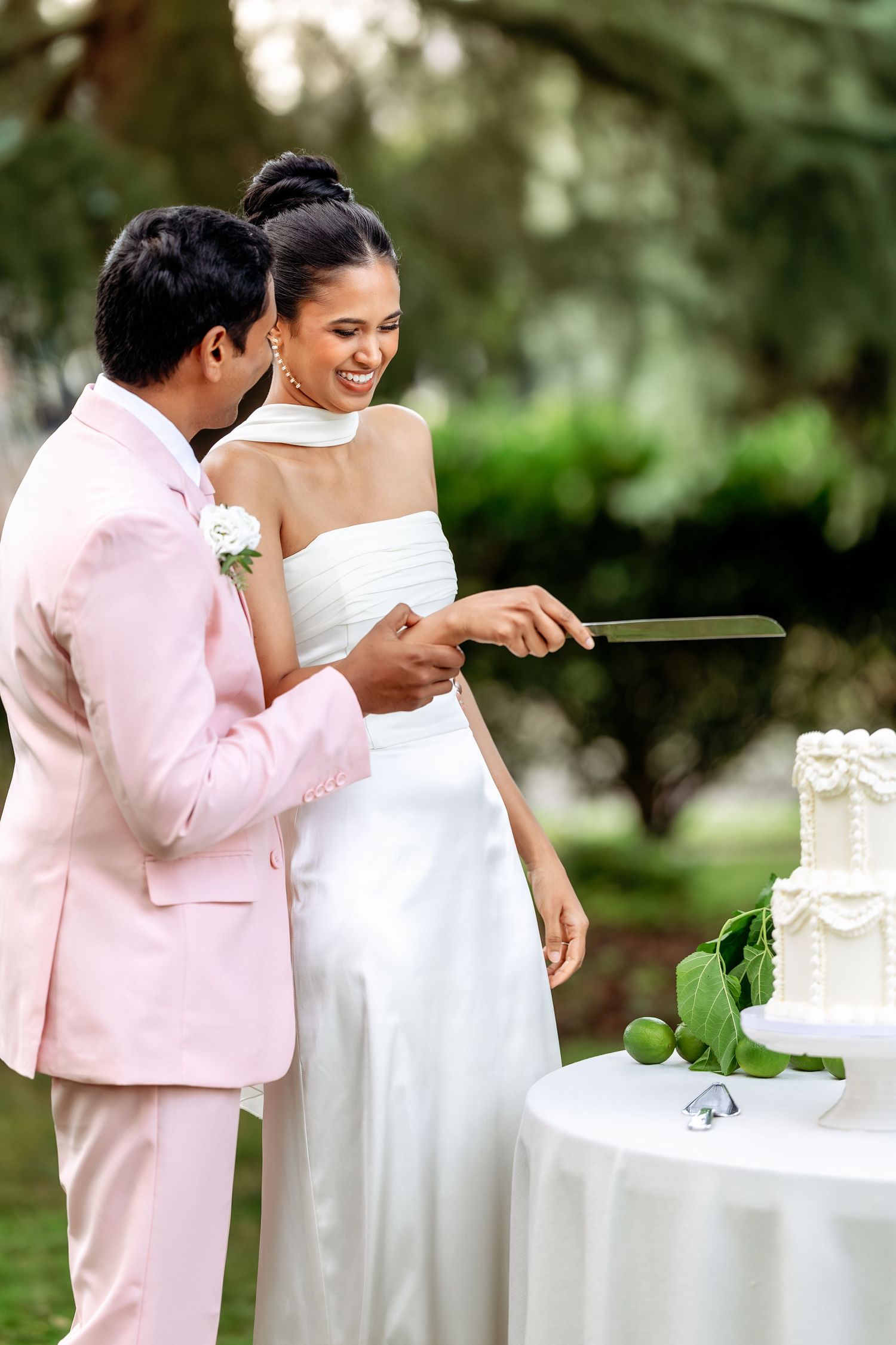 Wedding couple interacting with their tiered white cake at an outdoor reception.