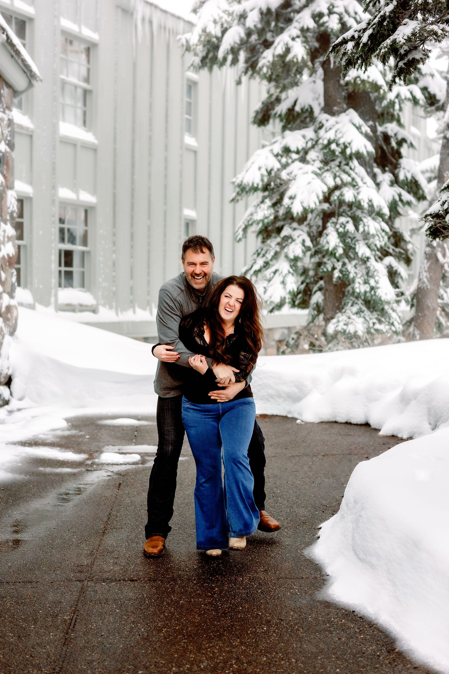 A couple shares a romantic moment together in a snowy winter setting with white buildings in the background.