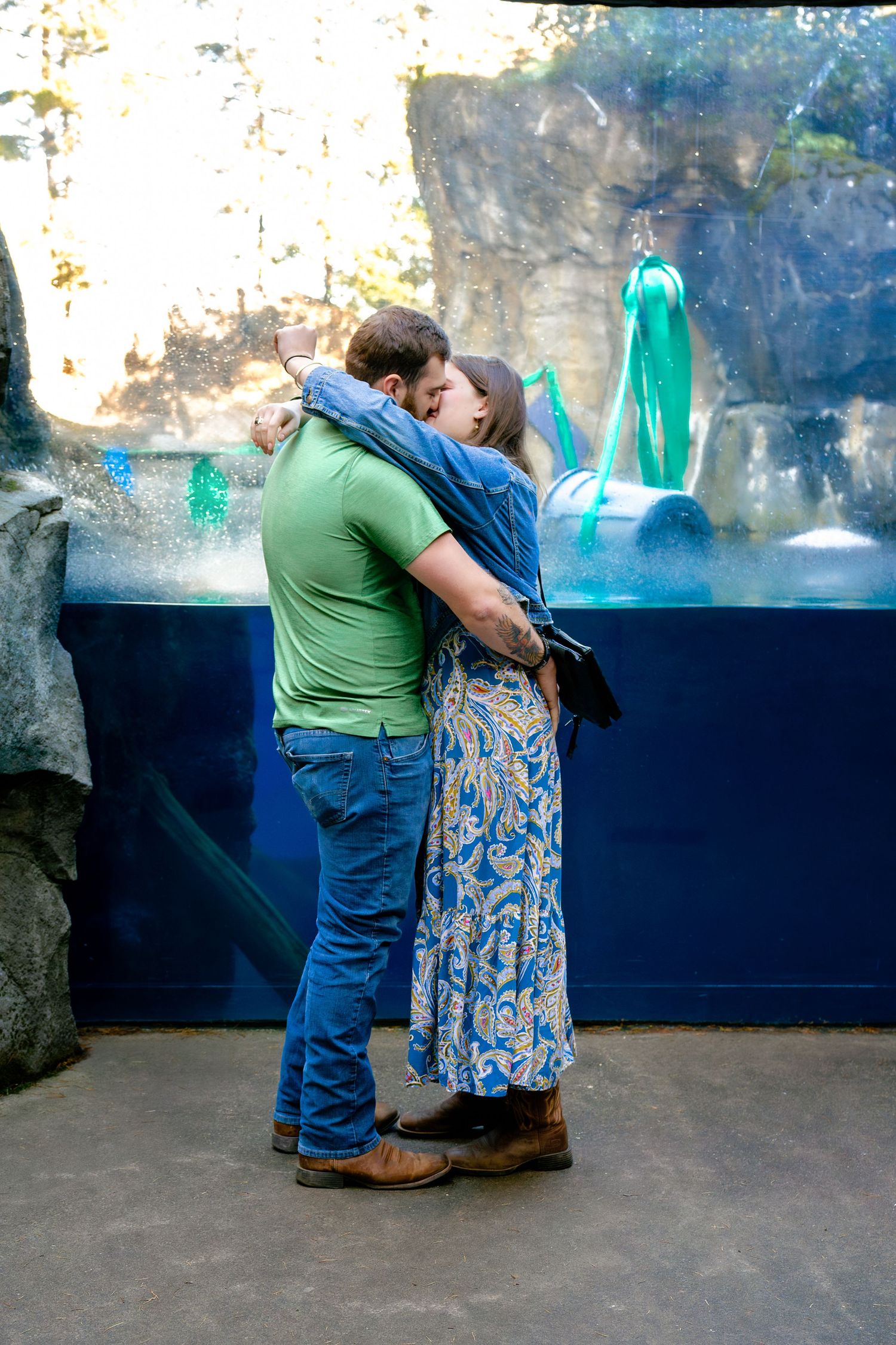 A couple looks at exhibits through glass panels in what appears to be an aquarium or zoo setting.