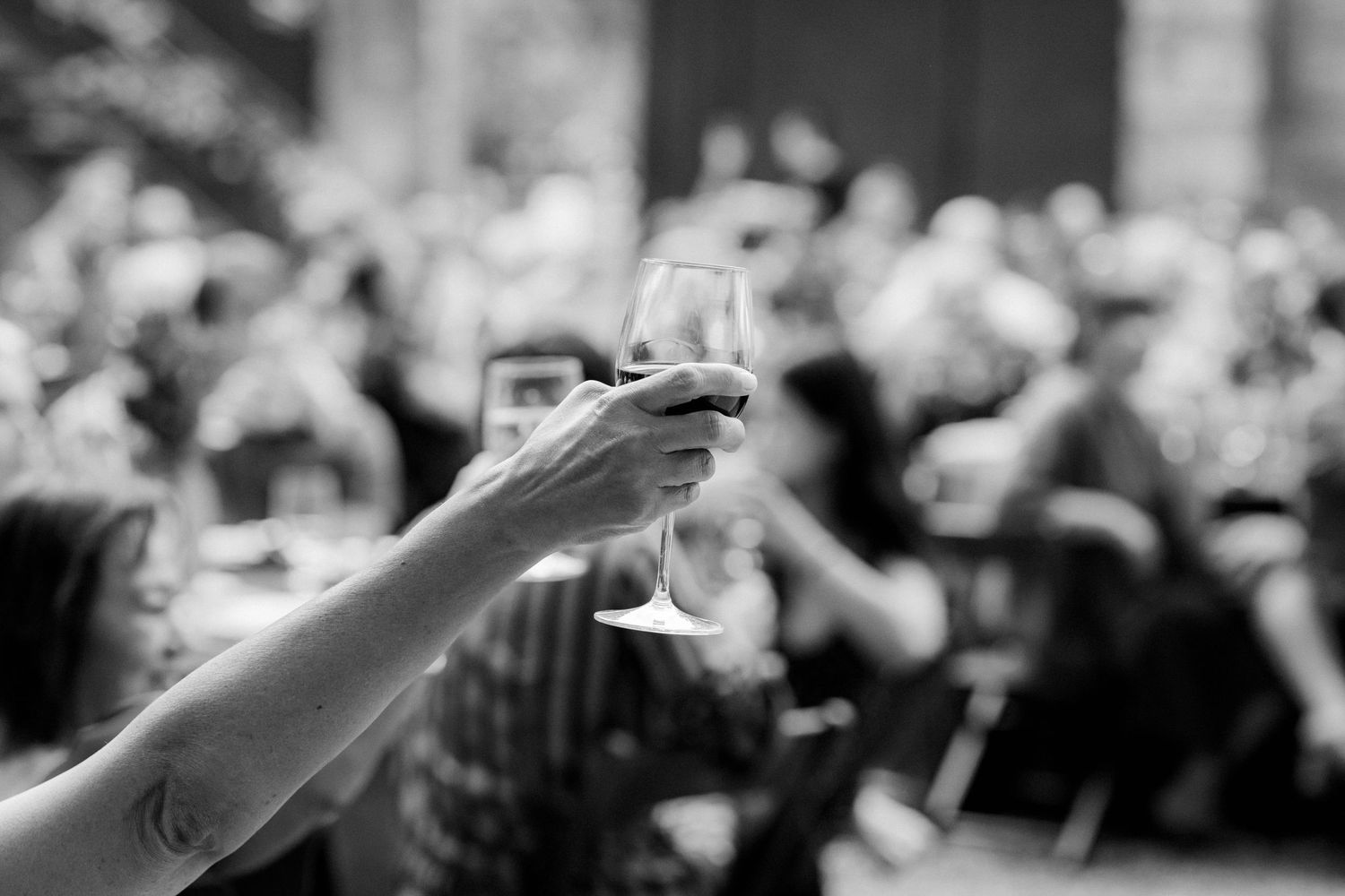 Black and white photo of a hand raising a champagne glass in a wedding toast.