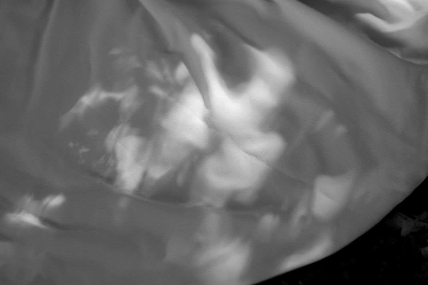 Abstract black and white photo of flowing fabric with soft light reflections creating dreamy cloud-like patterns.