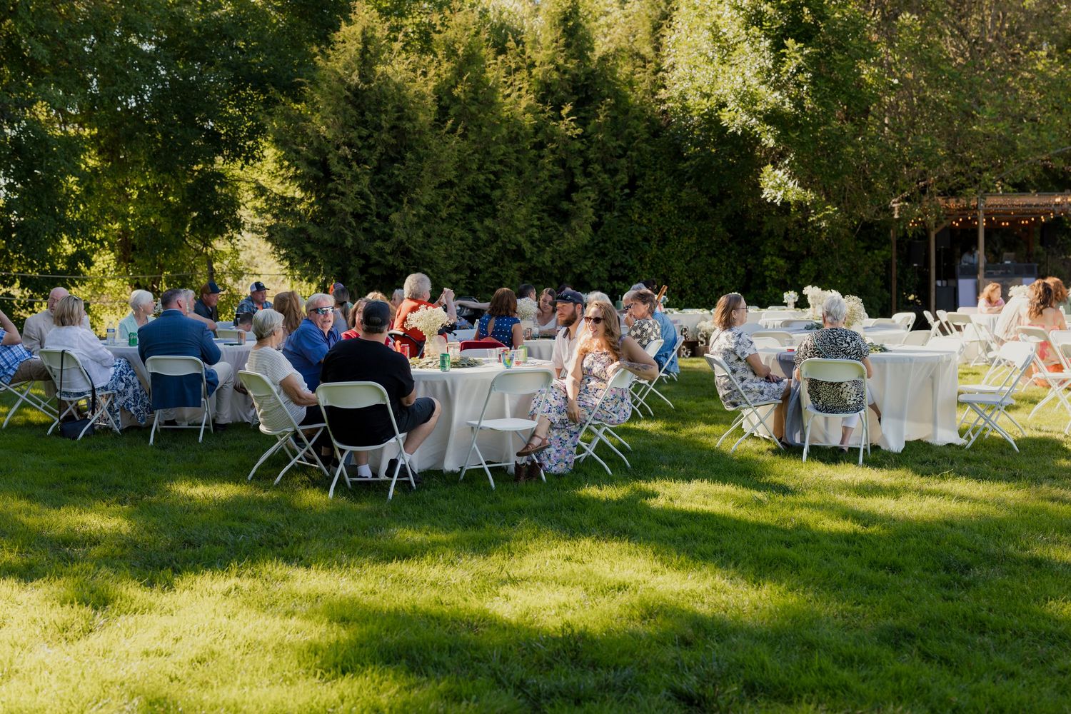 Wedding guests seated at round tables on green lawn during elegant outdoor garden reception.