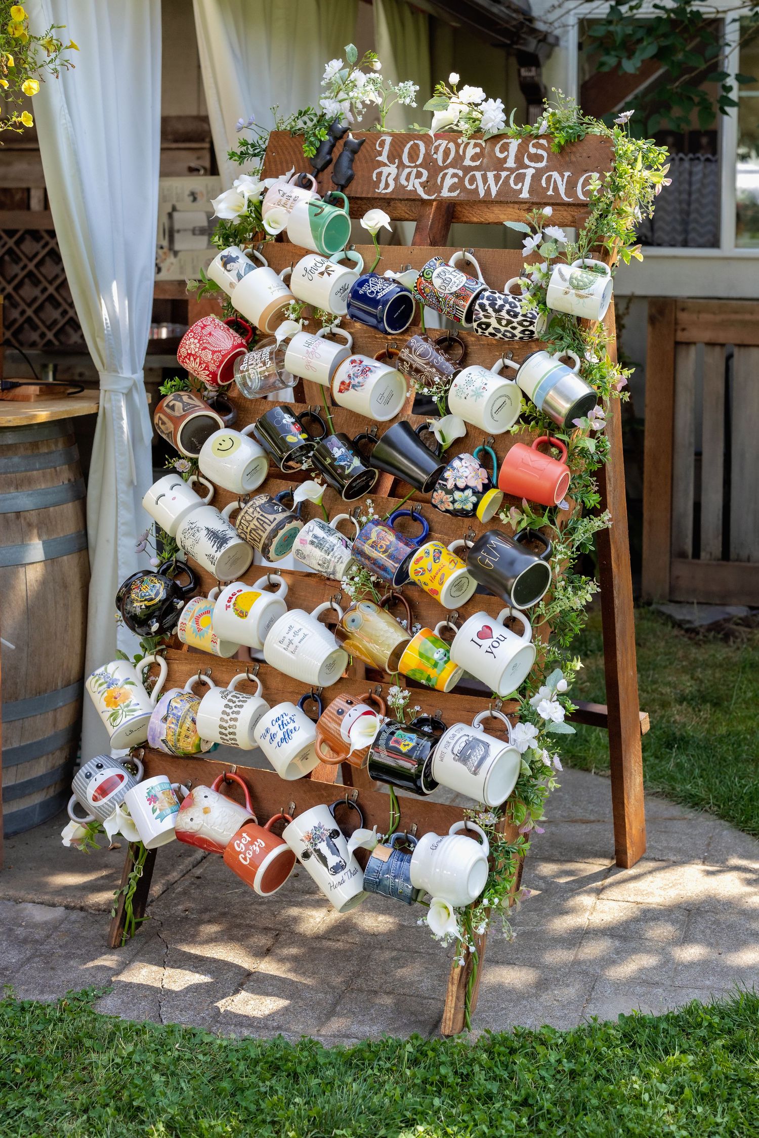 Rustic wooden display with vintage teacups and mugs arranged in cascading pattern with greenery and floral accents.