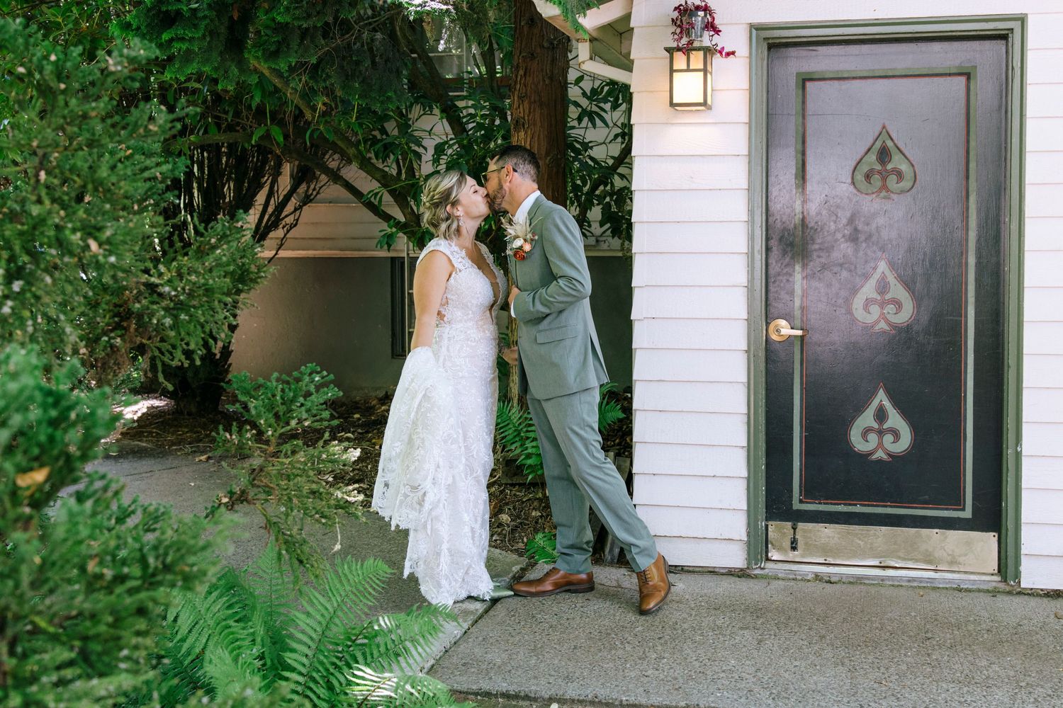 Newlyweds share intimate moment by decorated black door with spade designs.
