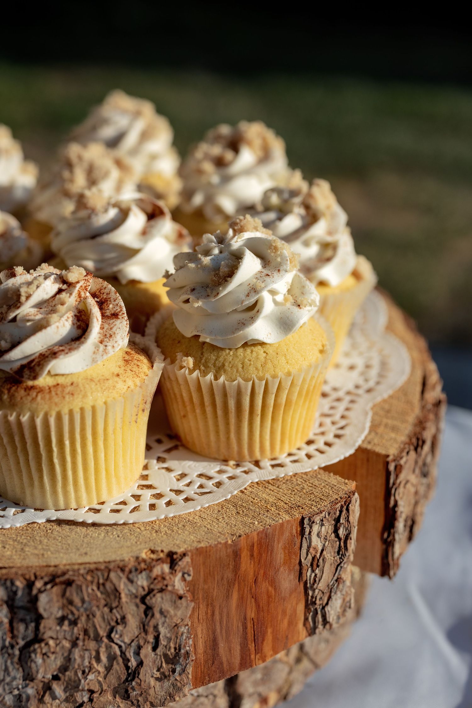 Homemade vanilla cupcakes with swirled buttercream frosting displayed on rustic wood slices and lace doilies.