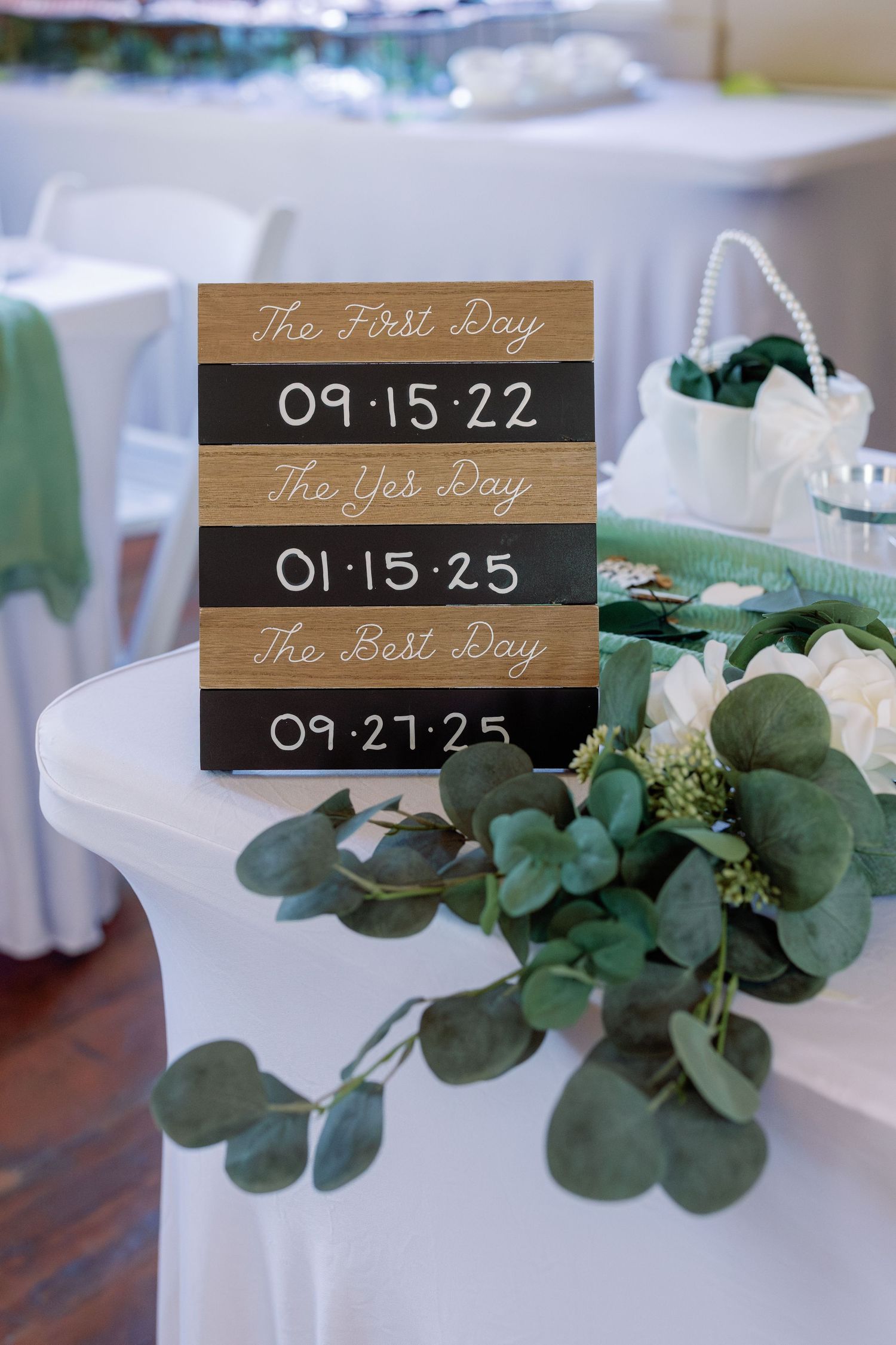 Wedding date signs on wooden blocks with eucalyptus greenery displaying significant dates.