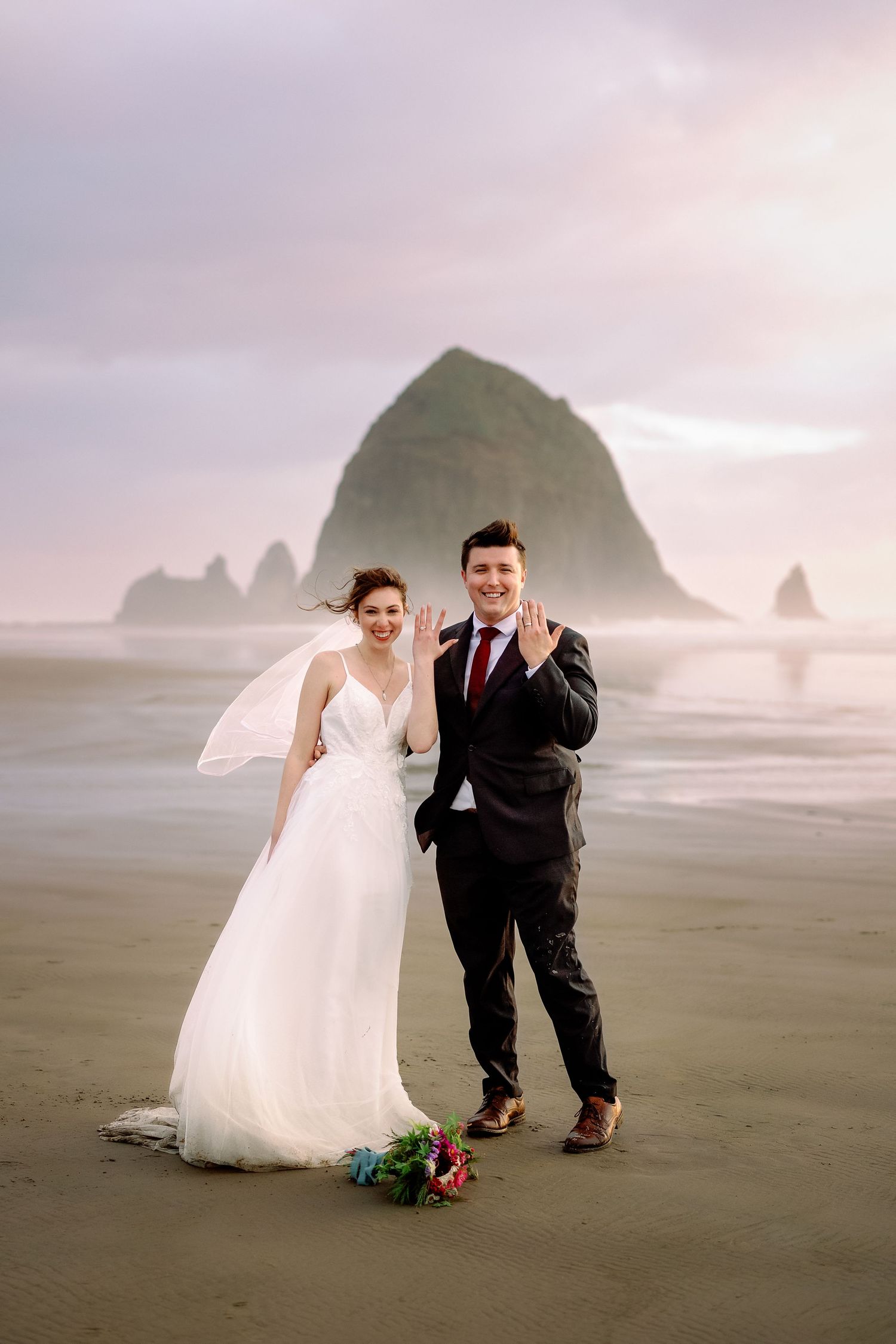 A couple shares a playful moment during their wedding photoshoot on the sandy shores of Cannon Beach, Oregon.