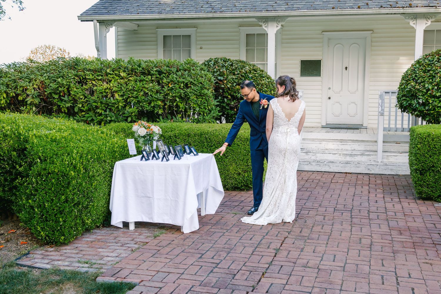 Outdoor wedding venue with brick pathway and white reception tables set up on the lawn.