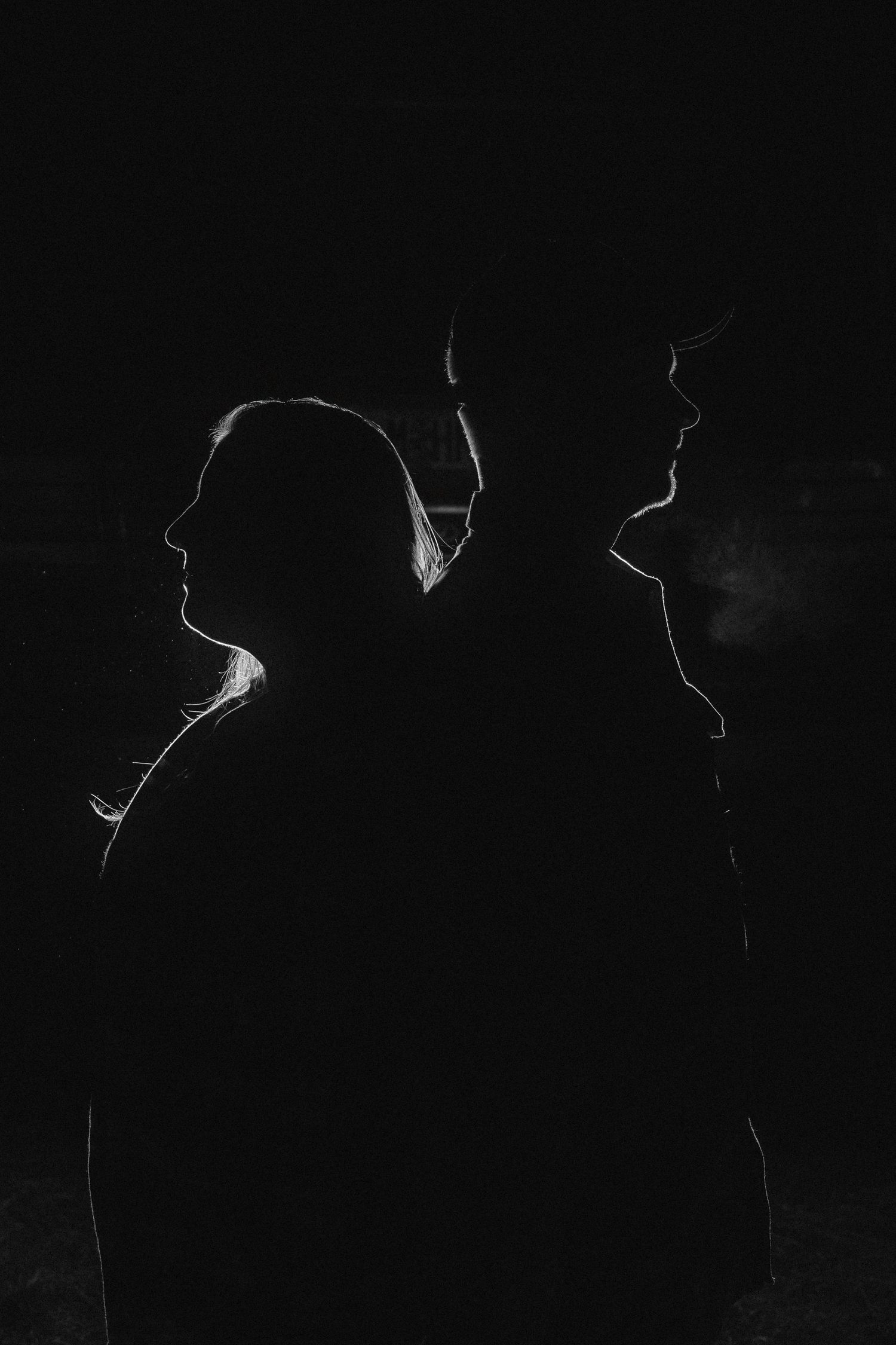 Silhouettes of figures stand in darkness against a black background creating a mysterious atmospheric scene.