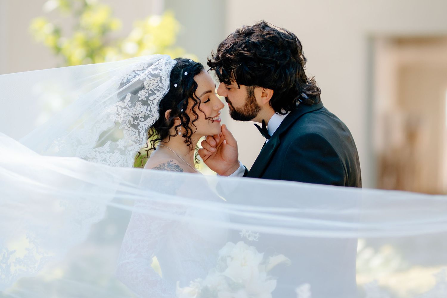 Bride and groom sharing a romantic kiss under a flowing white veil on their wedding day.
