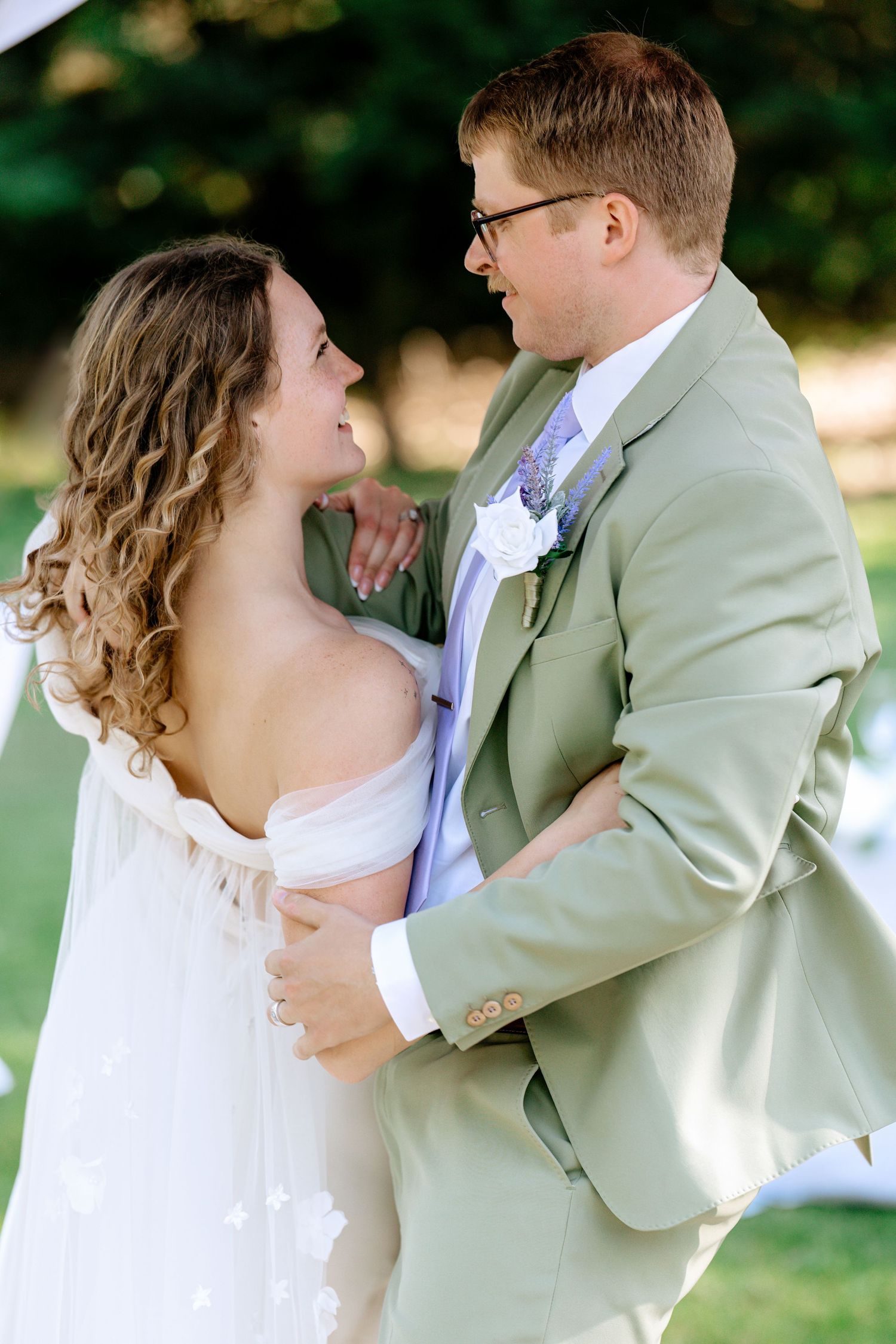 Bride and groom gaze lovingly at each other while embracing at their outdoor garden wedding ceremony.