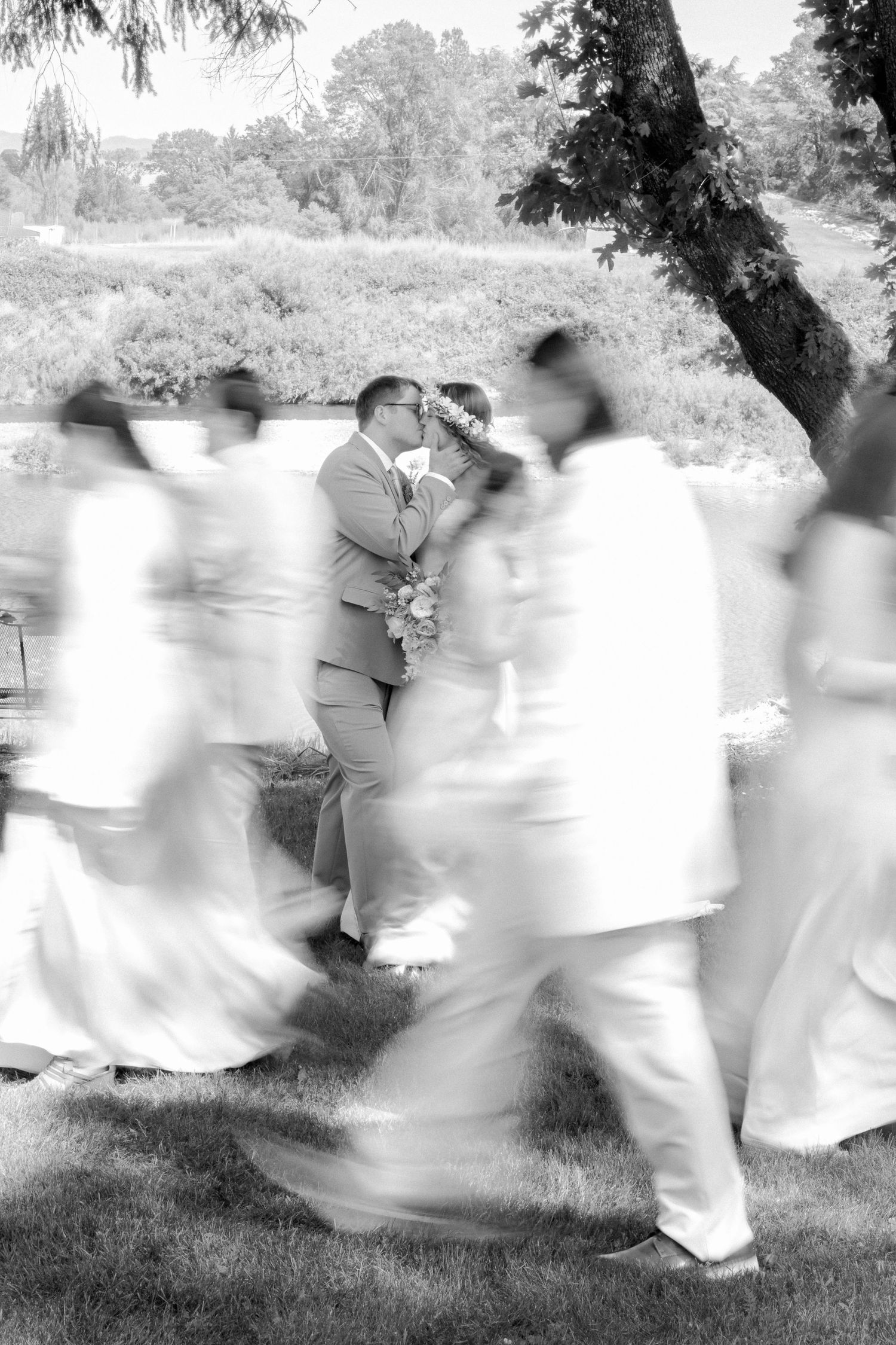 Black and white photo of bride and groom kissing as wedding party walks past in a motion blur effect.