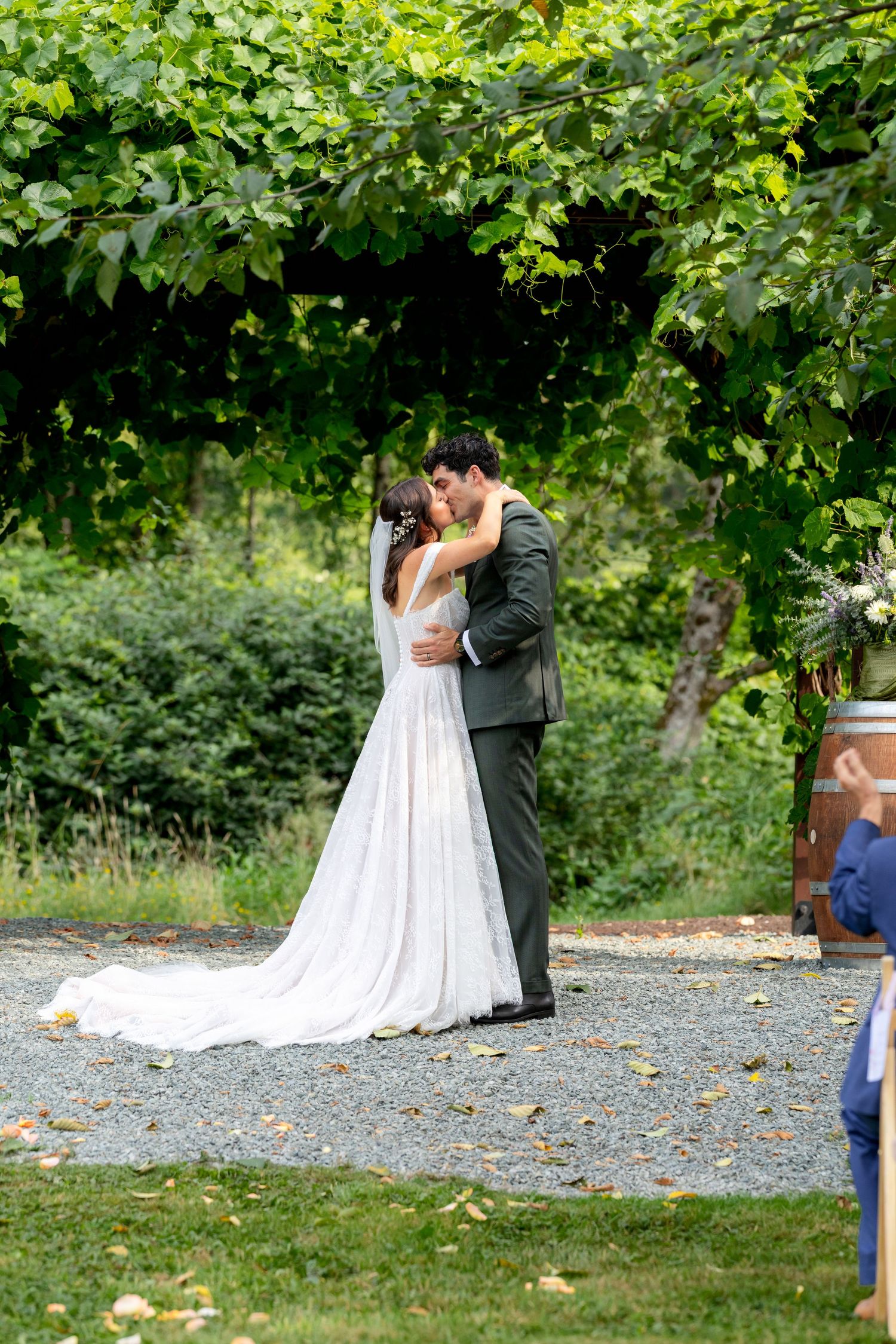 Bride and groom share their first kiss outdoors under lush green vines at an elegant garden wedding ceremony.