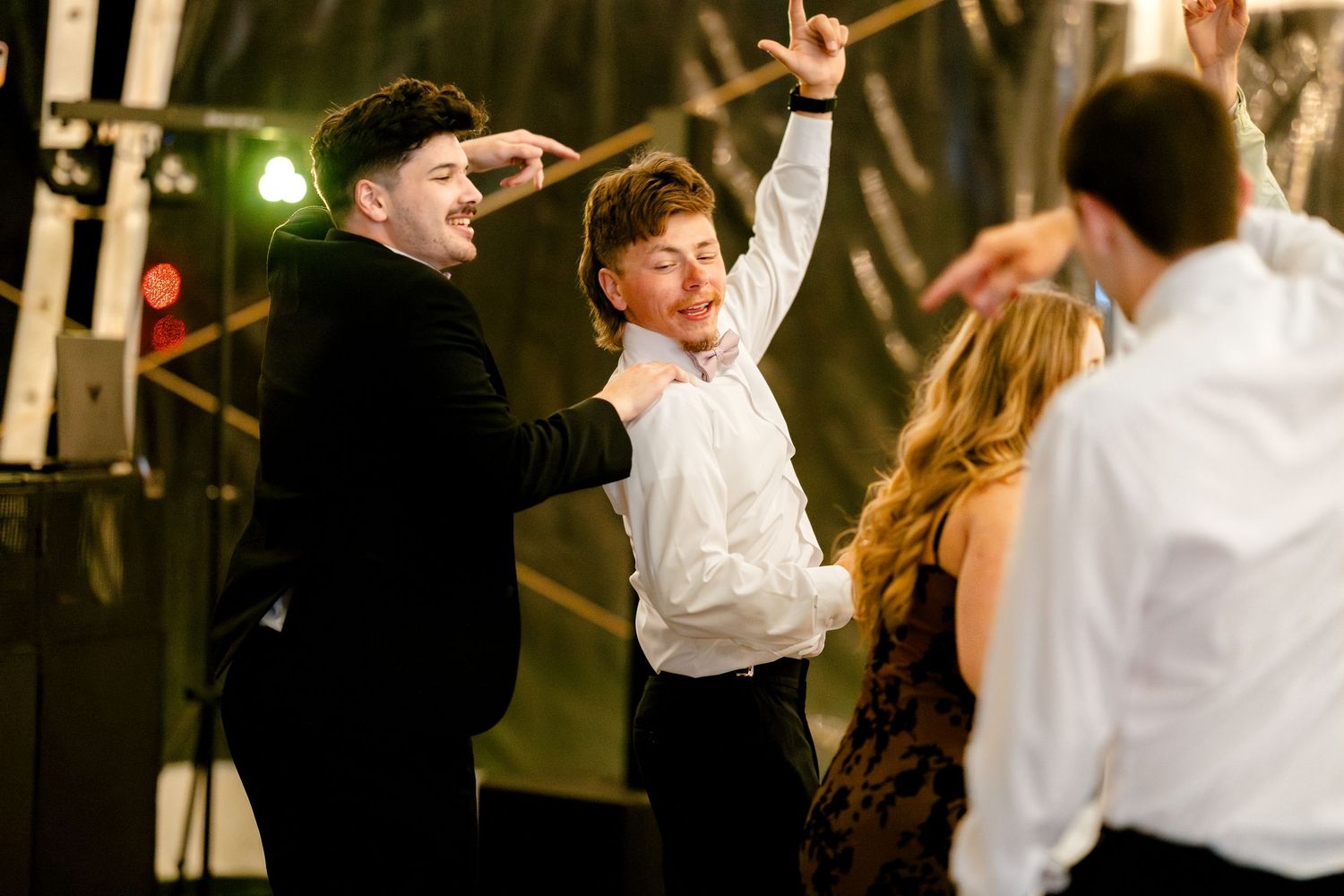 A lively dance party scene with people in formal attire dancing under warm lighting at an indoor venue.