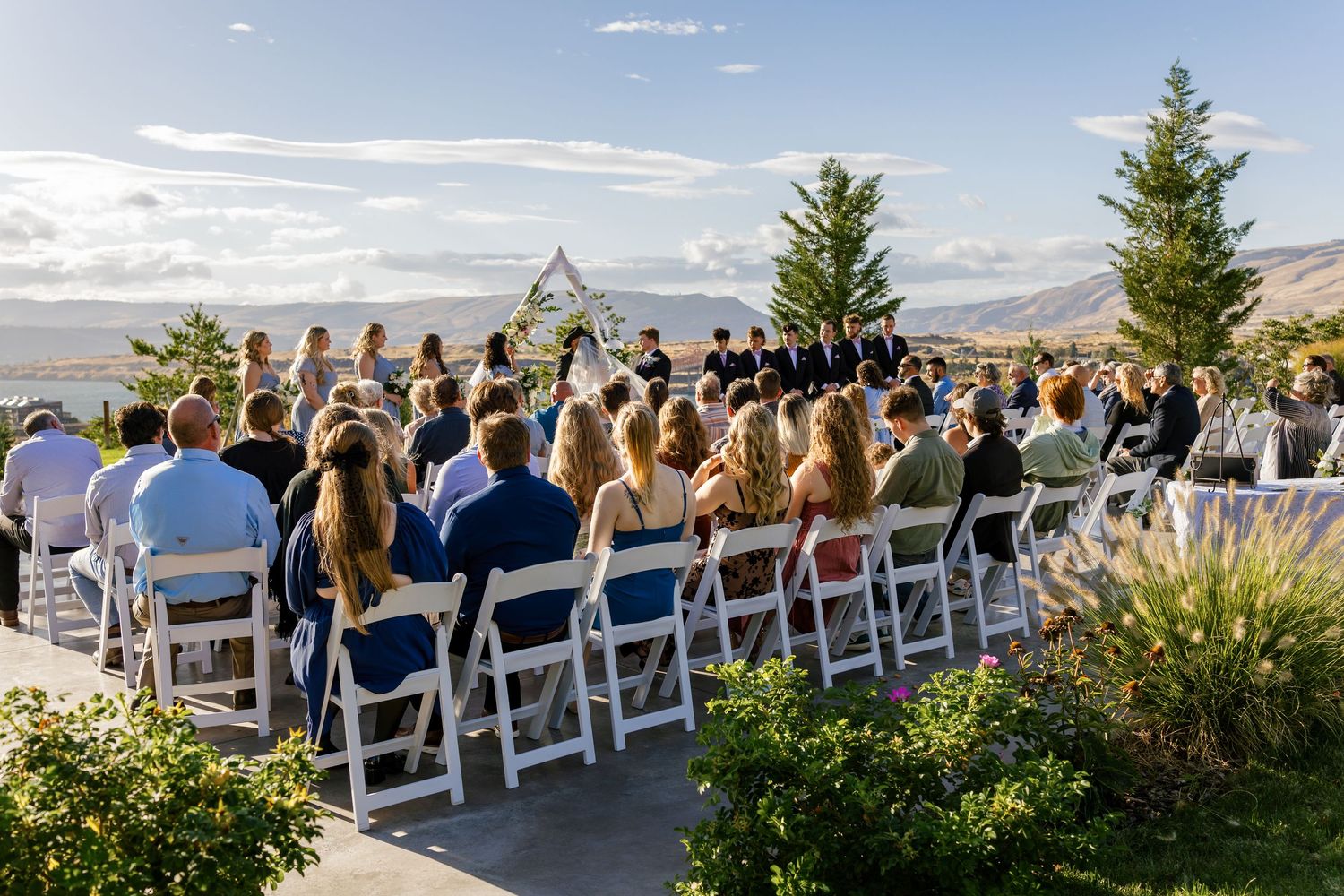 Outdoor wedding ceremony setup with white chairs facing mountain vista.