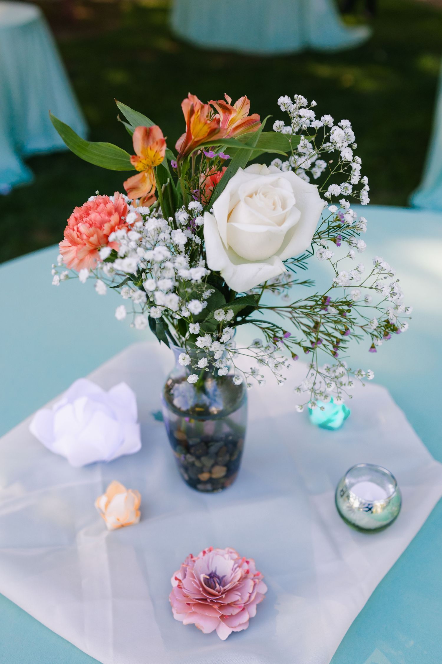 Delicate floral centerpieces with pink and white flowers in small vases arranged on a light blue tablecloth.