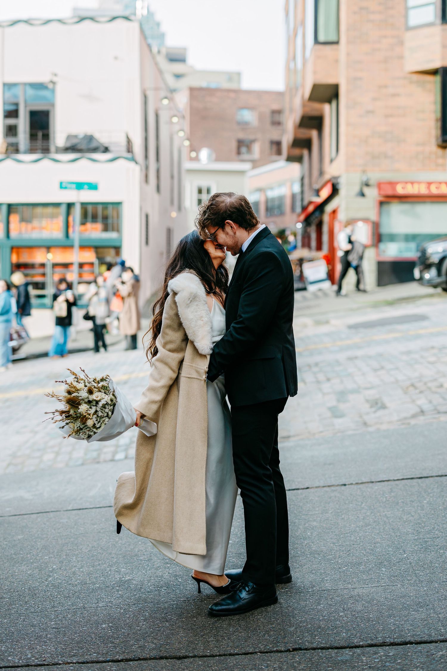 A couple in formal attire embracing on a city street during a photo session.