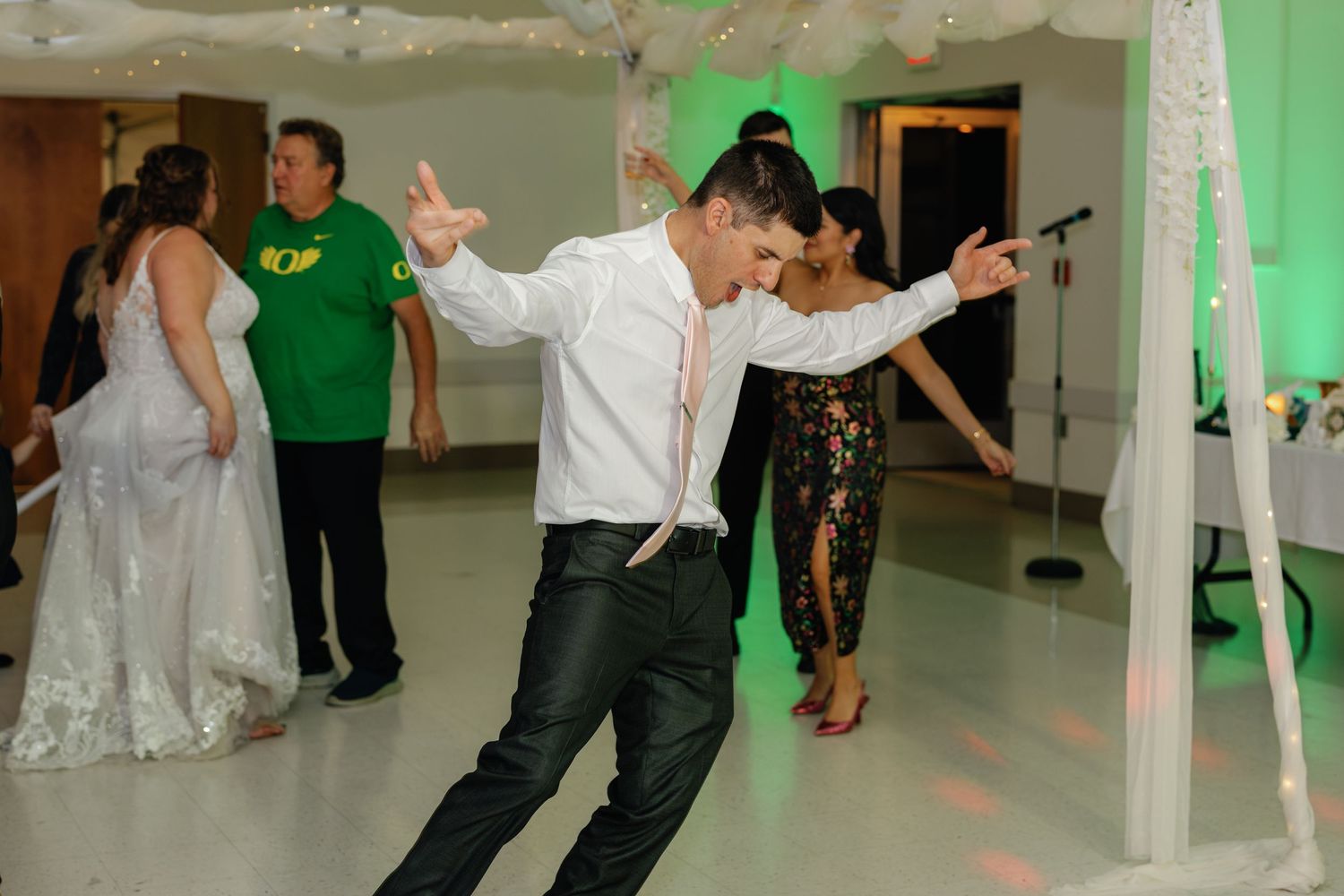 Wedding guests dancing and celebrating on illuminated dance floor with green accent lighting.