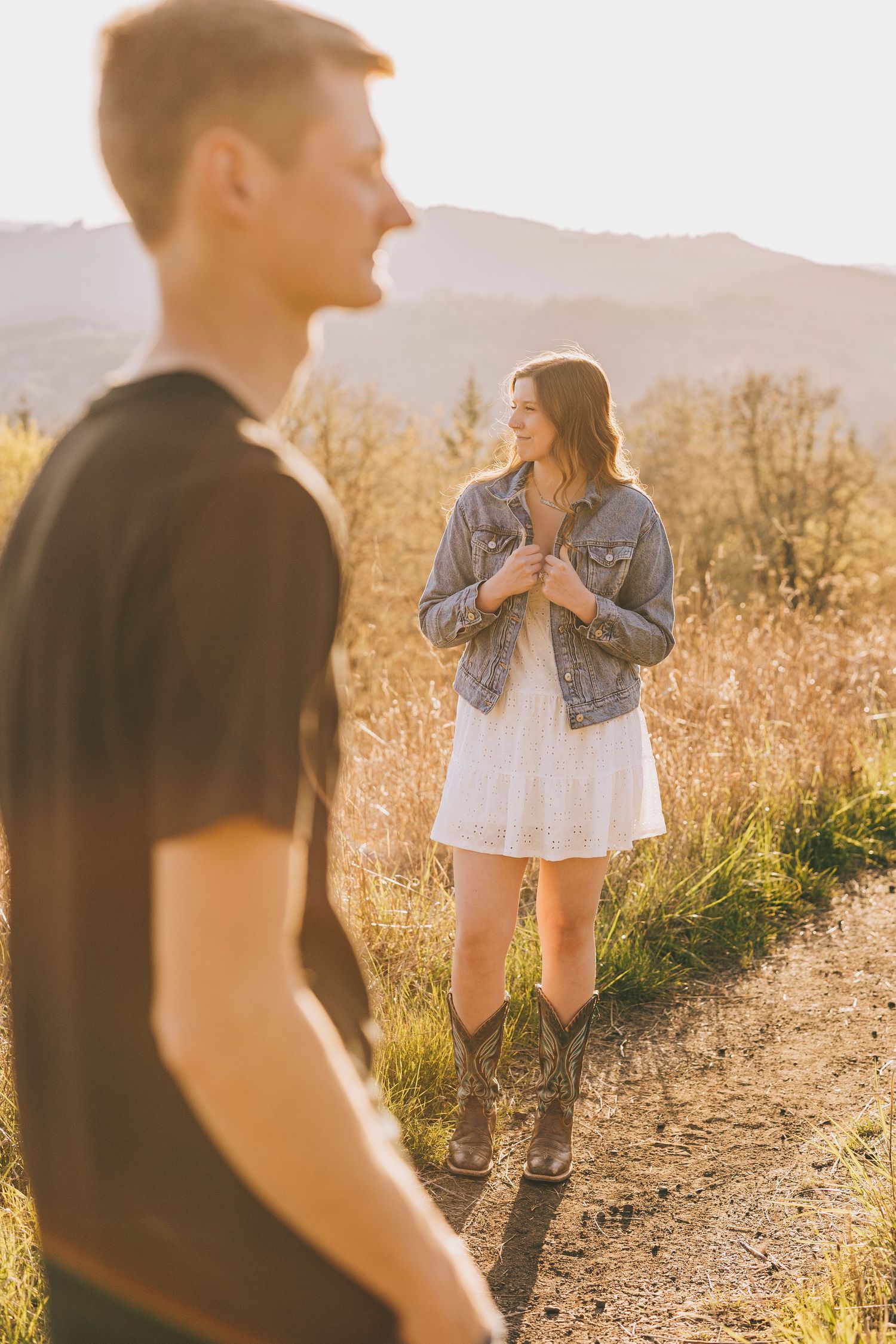 A couple shares a playful moment on a mountain trail during golden hour.