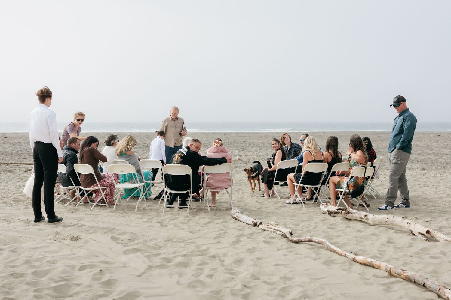 A beach wedding ceremony setup with folding chairs and guests gathered on the sand.