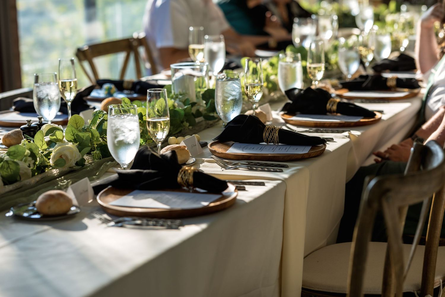 Elegant wedding reception table settings with dark plates, wine glasses, and natural greenery centerpieces.