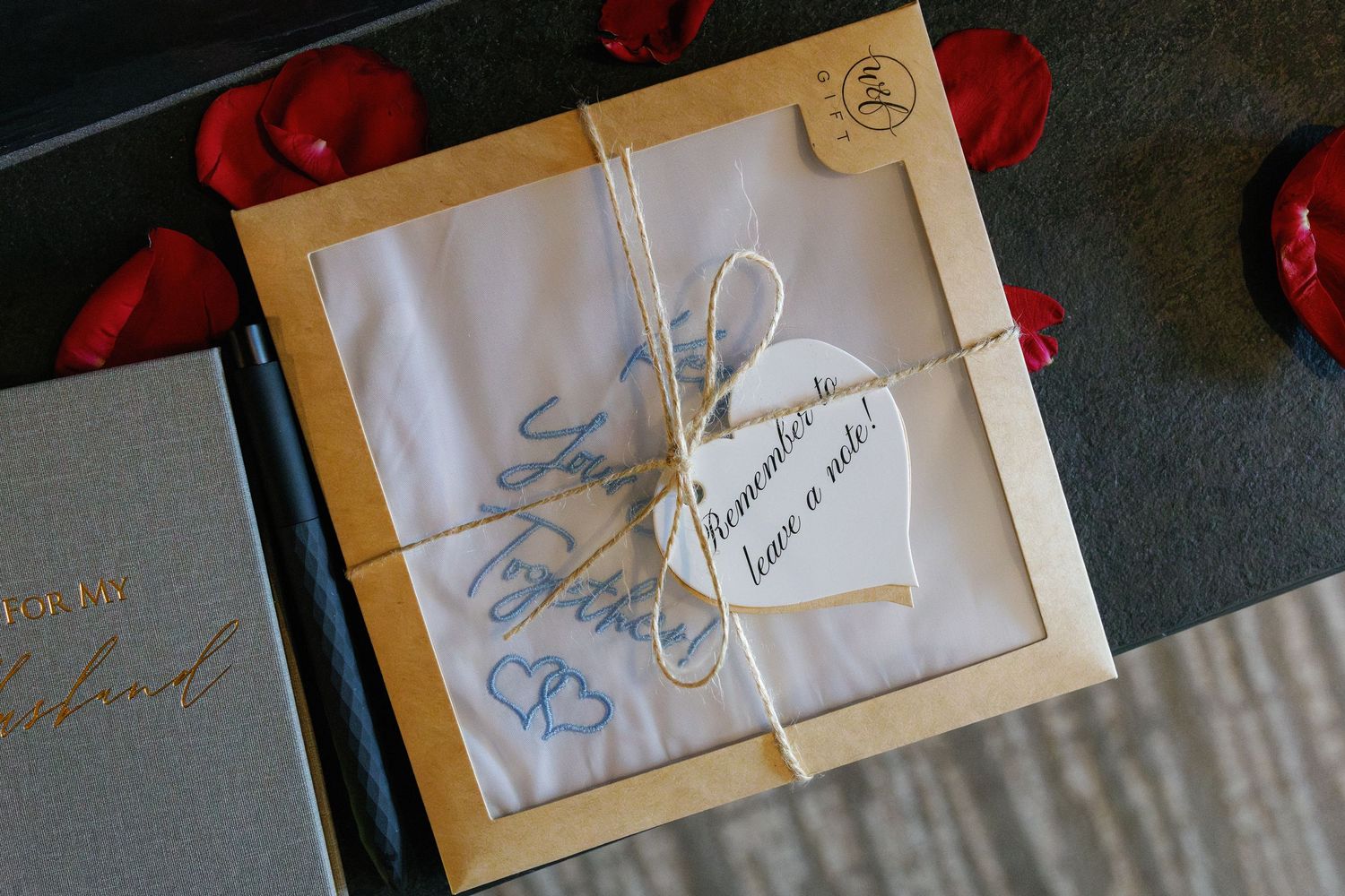 Wedding invitation with twine and a small tag tied around it, surrounded by red rose petals.