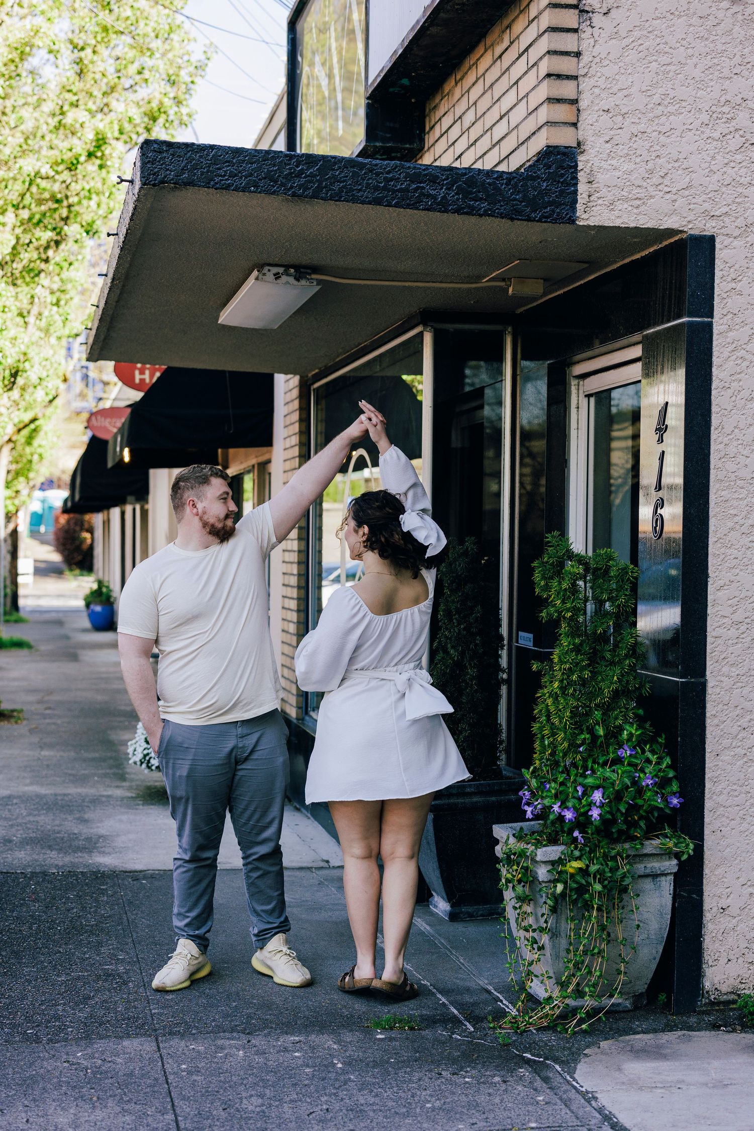 A couple poses playfully outside a brick building with an awning.