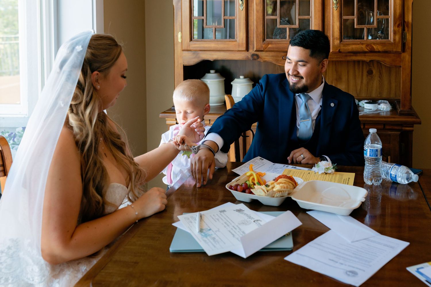 Bride and groom in blue suit share a joyful moment with their baby at a dining table.