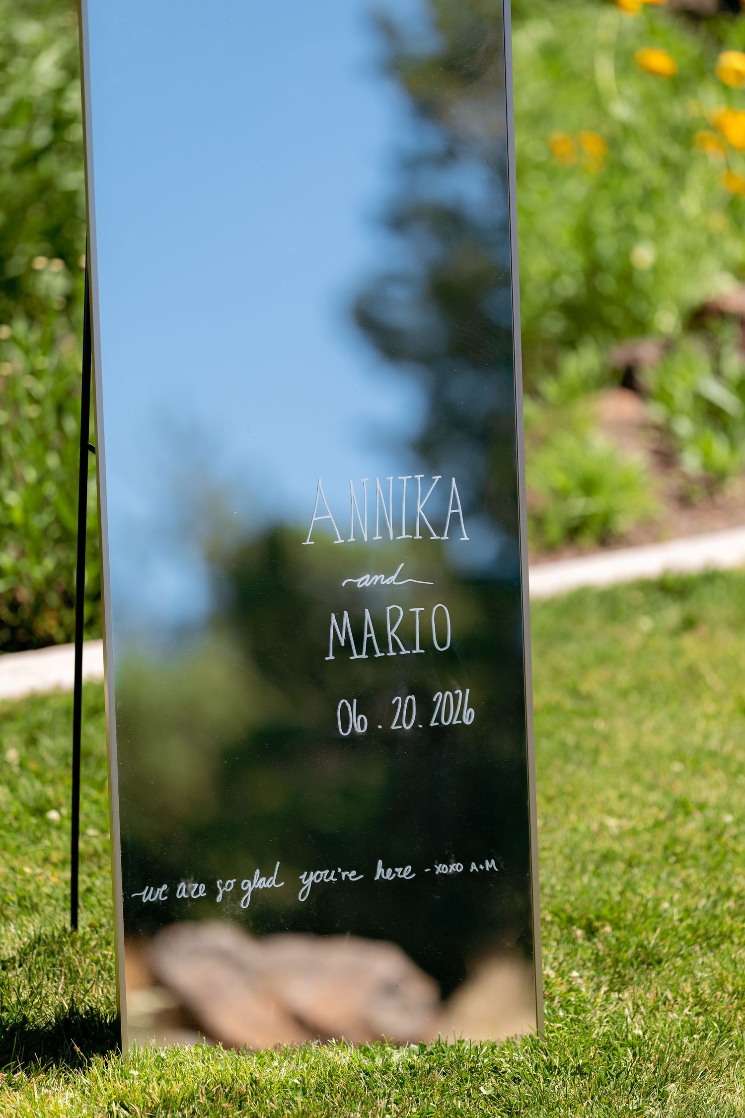 Elegant mirror wedding welcome sign for Annika and Mario dated 06.20.2026 on green lawn.