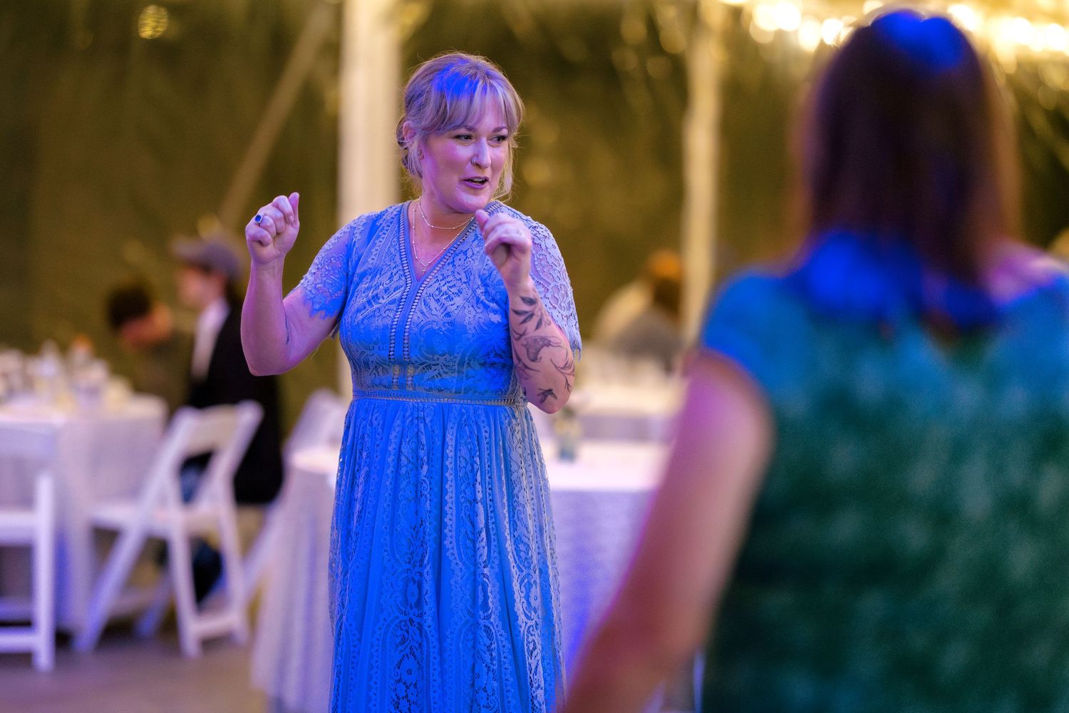 Wedding reception scene with guests in bright blue dresses under evening lighting.