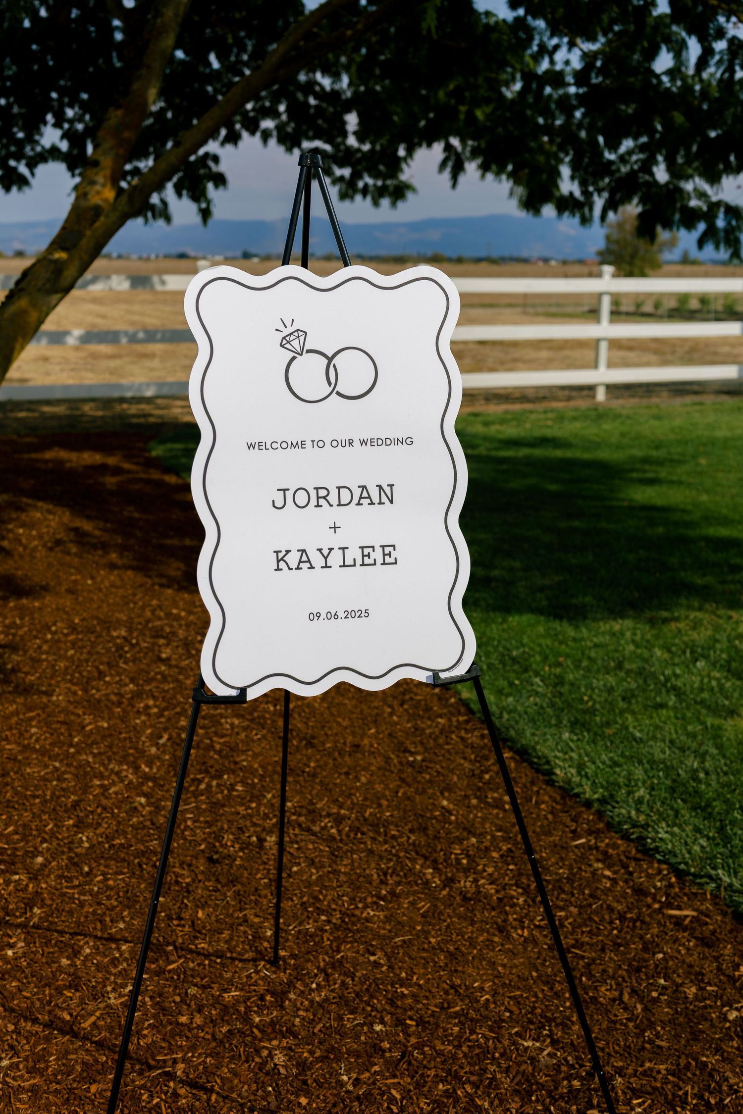 Wedding welcome sign with interlocking rings design displayed on an easel outdoors.