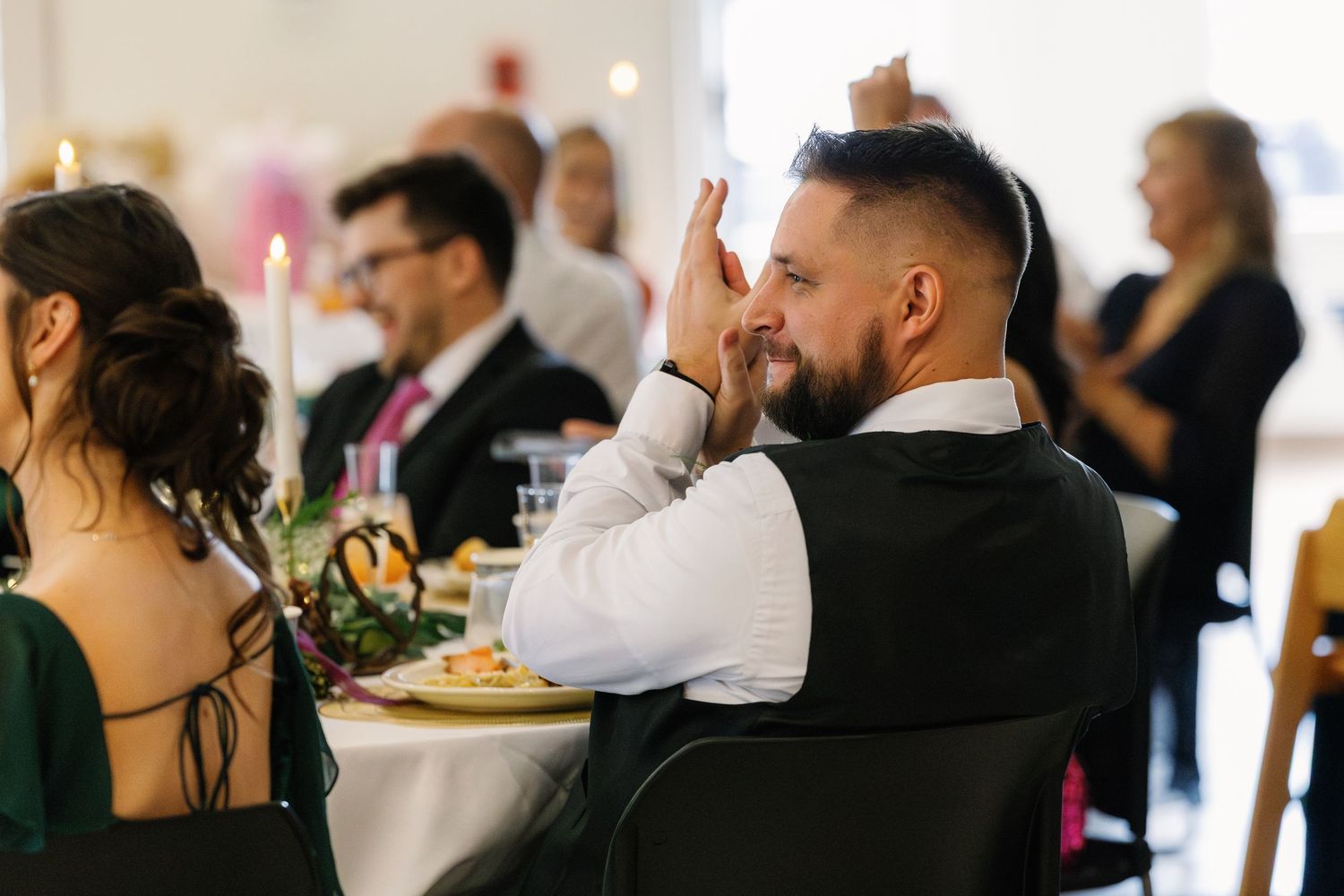 Wedding guest in a vest enjoying dinner and raising his hand at a reception celebration.