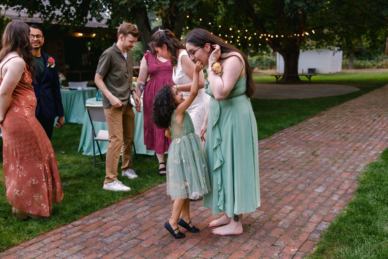 Wedding guests dance and celebrate on a brick patio surrounded by string lights and greenery during an outdoor reception.