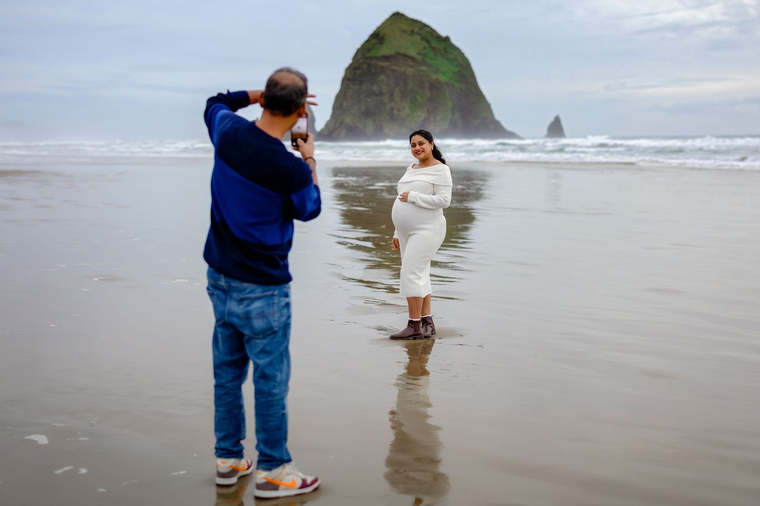 A person walks along the misty shoreline of Cannon Beach, Oregon with Haystack Rock visible in the background.