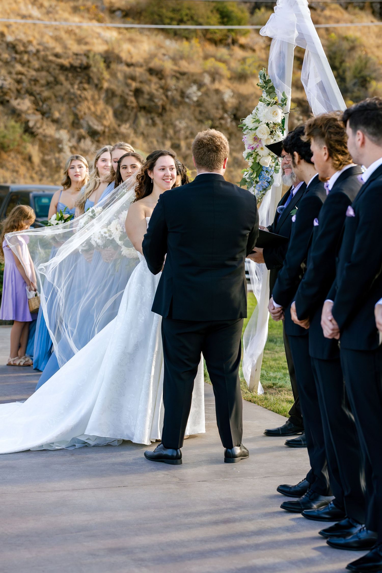 Wedding ceremony processional with bridal party in formal attire walking down outdoor aisle.