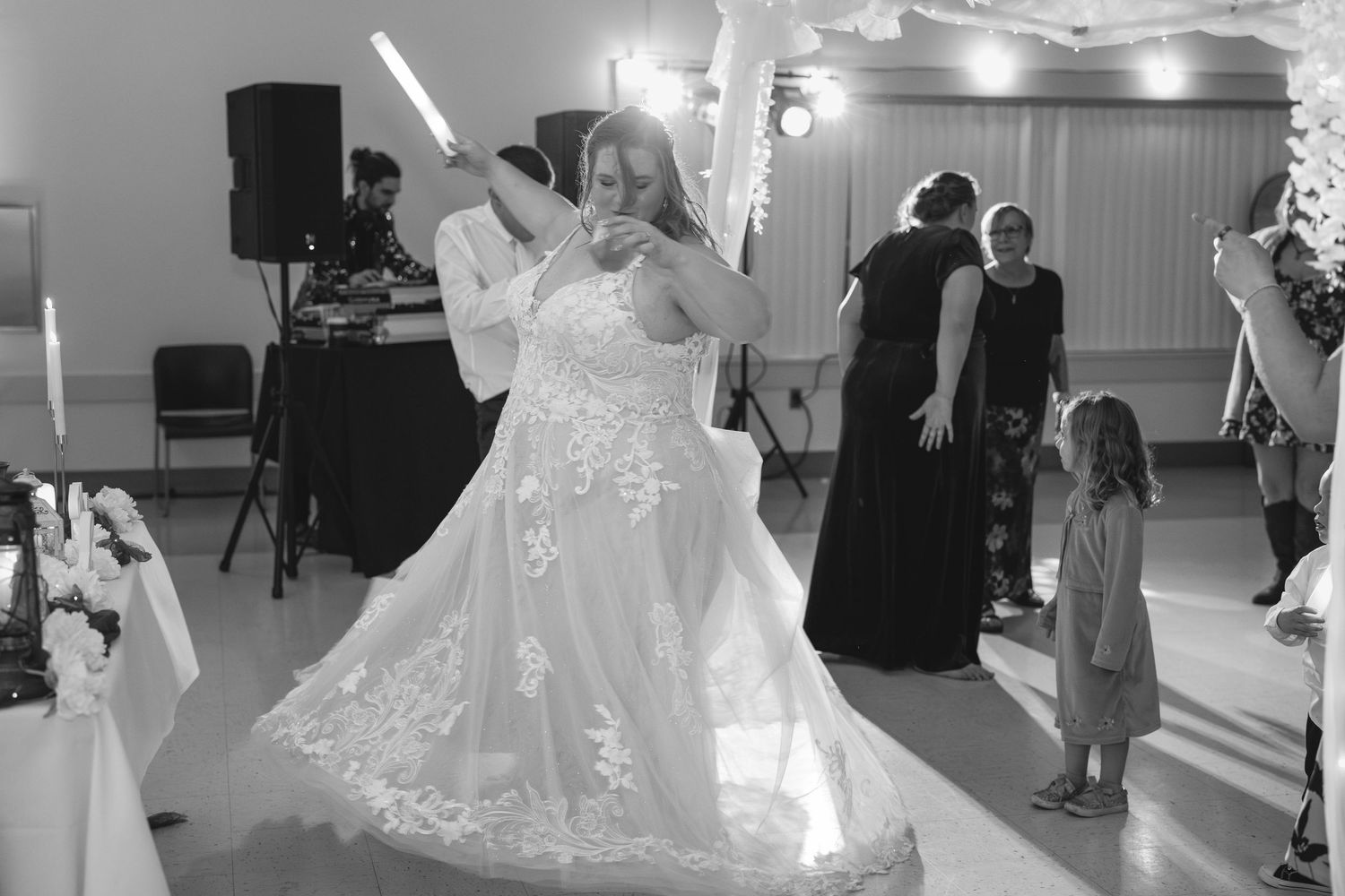 A black and white photo of a couple dancing their first dance at a wedding reception with guests watching.