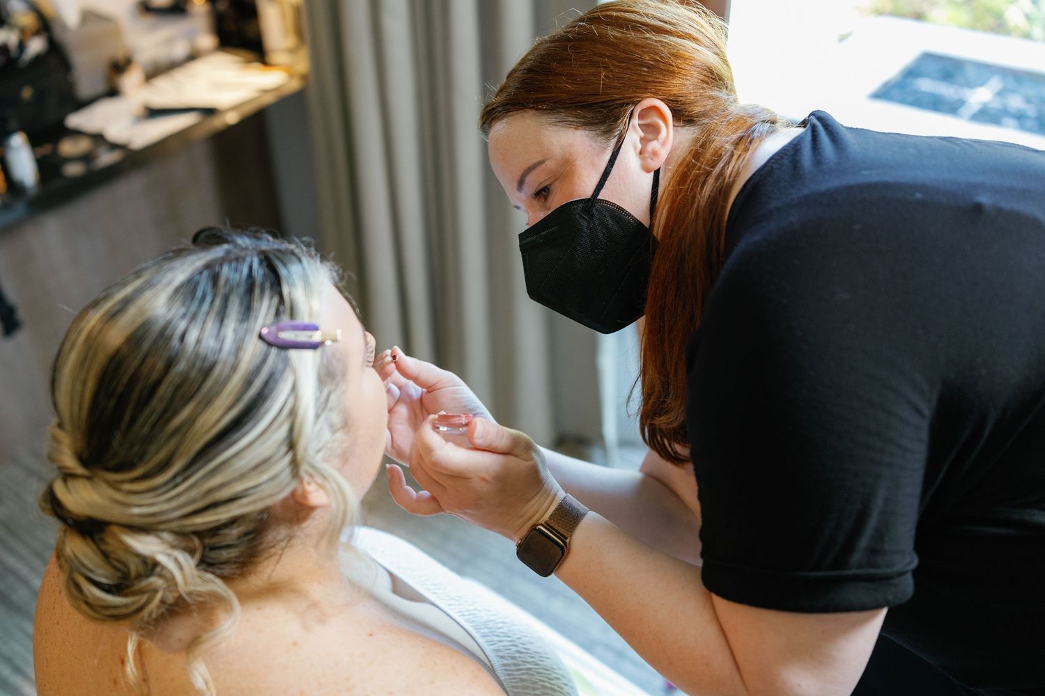 Professional makeup artist applies cosmetics to a client during a bridal preparation session.